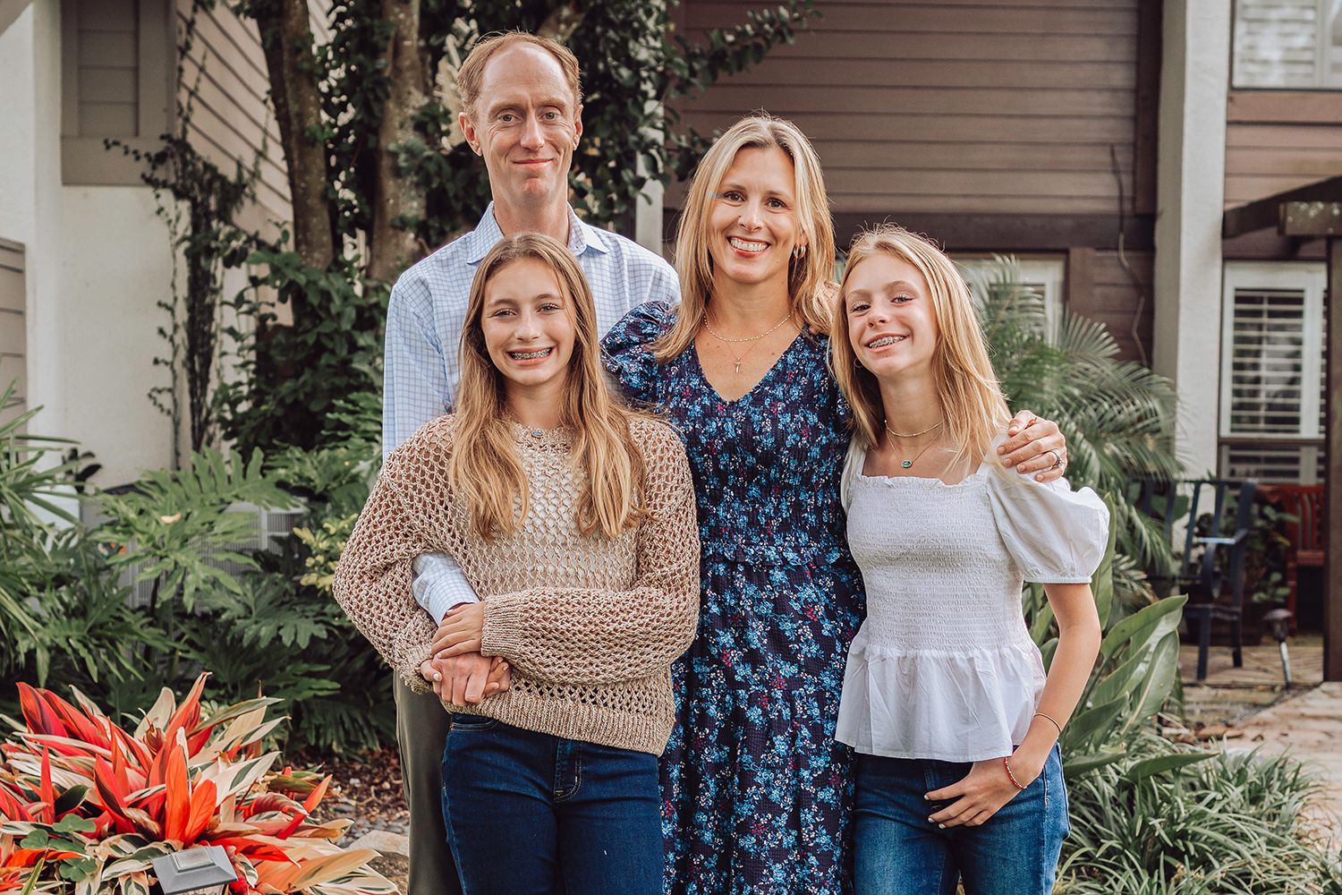 A family group poses together outdoors in coordinated casual outfits near a house with landscaping in Jacksonville Florida