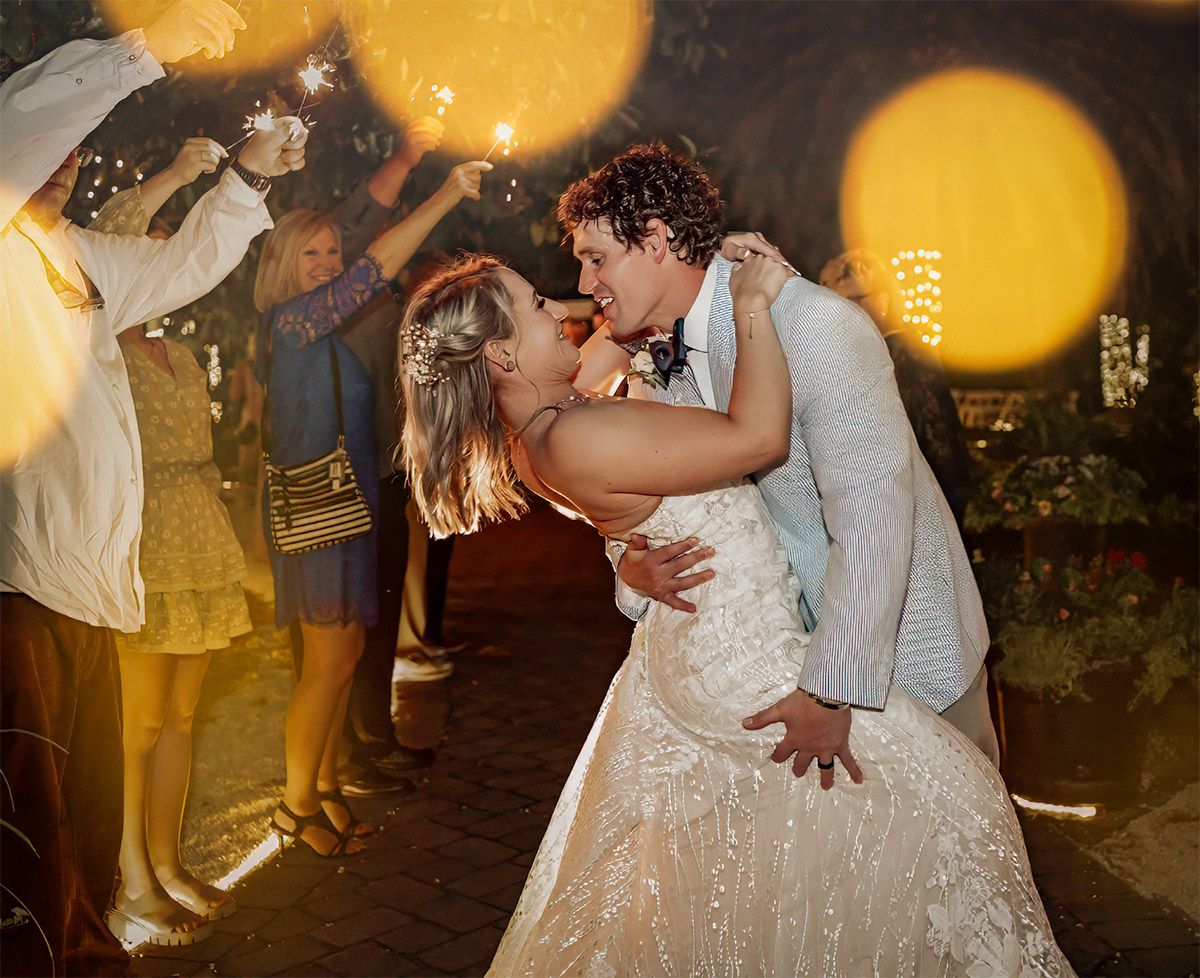 Romantic couple shares an intimate dance at a wedding reception with warm golden lighting and bokeh effects in background.