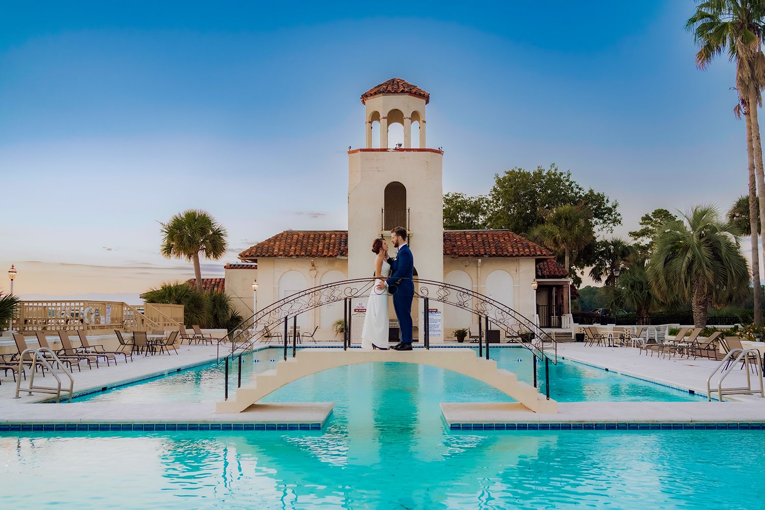 Panoramic view of pool with turquoise water and palm trees against a bright blue sky for wedding photographer in Savannah.