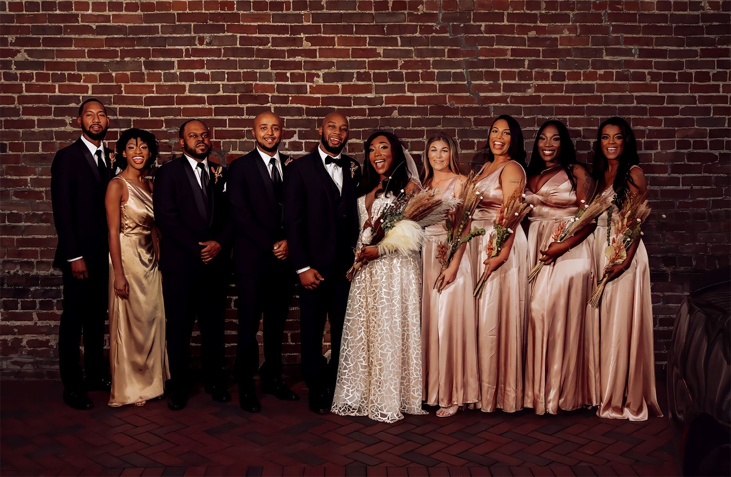A wedding party poses for photos against a rustic brick wall in formal attire for wedding photographer in Jacksonville, Florida.