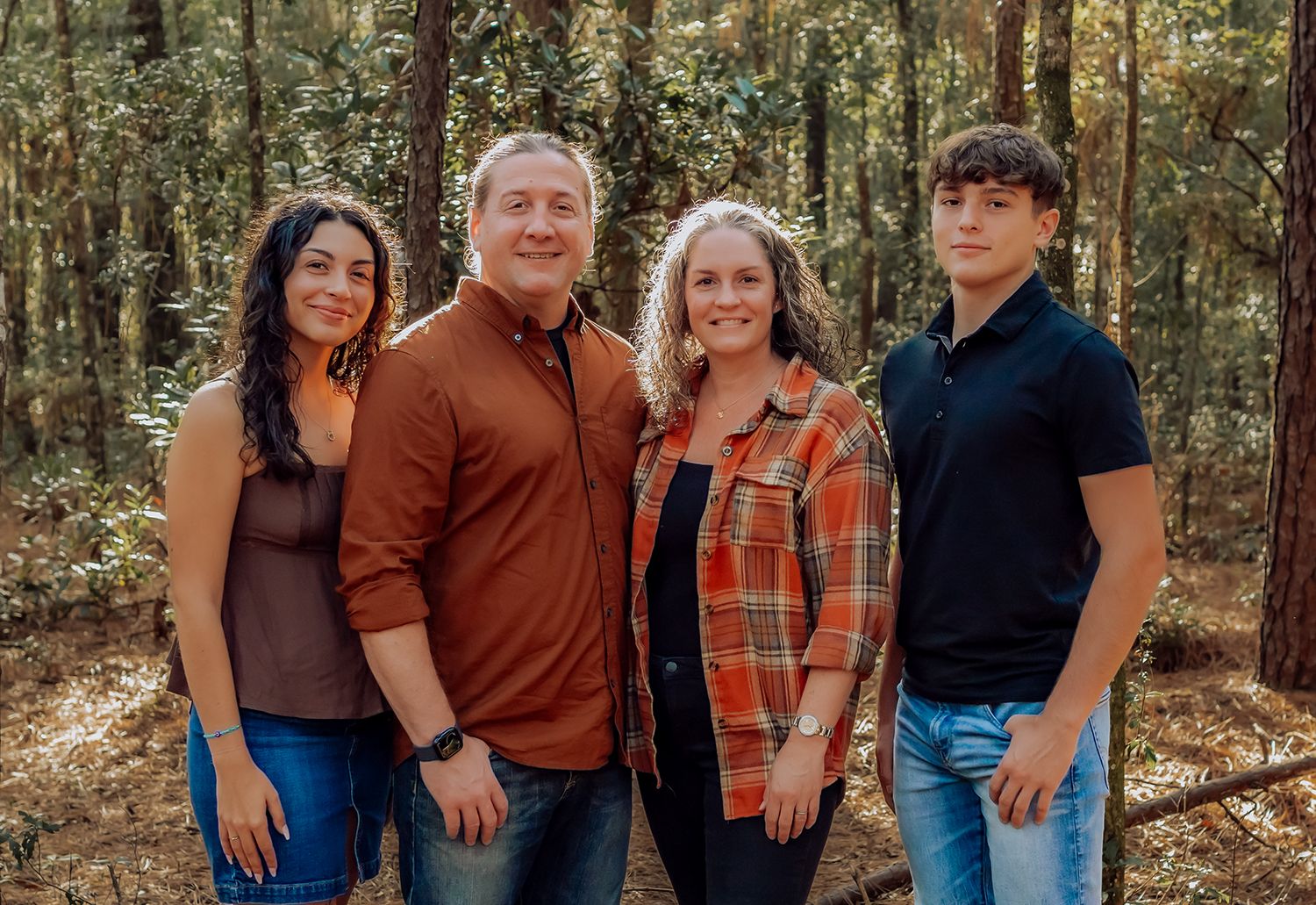 Group portrait in autumn forest setting with coordinated casual outfits in earth tones and plaid patterns for family photos in Gainesville