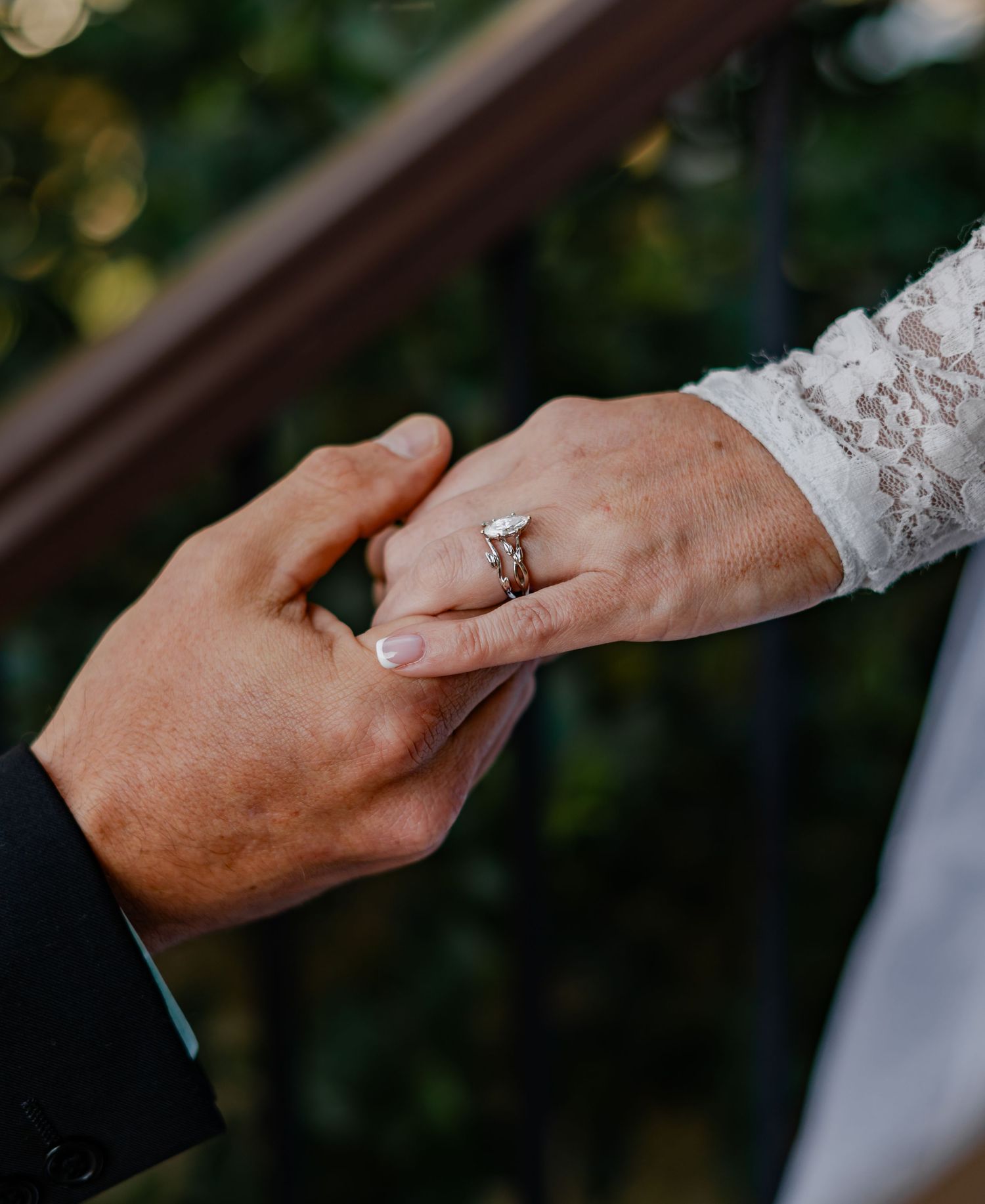 Groom placing a diamond engagement ring on bride's finger during wedding ceremony, with lace sleeve visible.