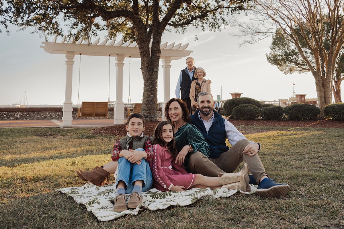 Family relaxes together on picnic blanket at sunset in grassy field during outdoor photo session.
