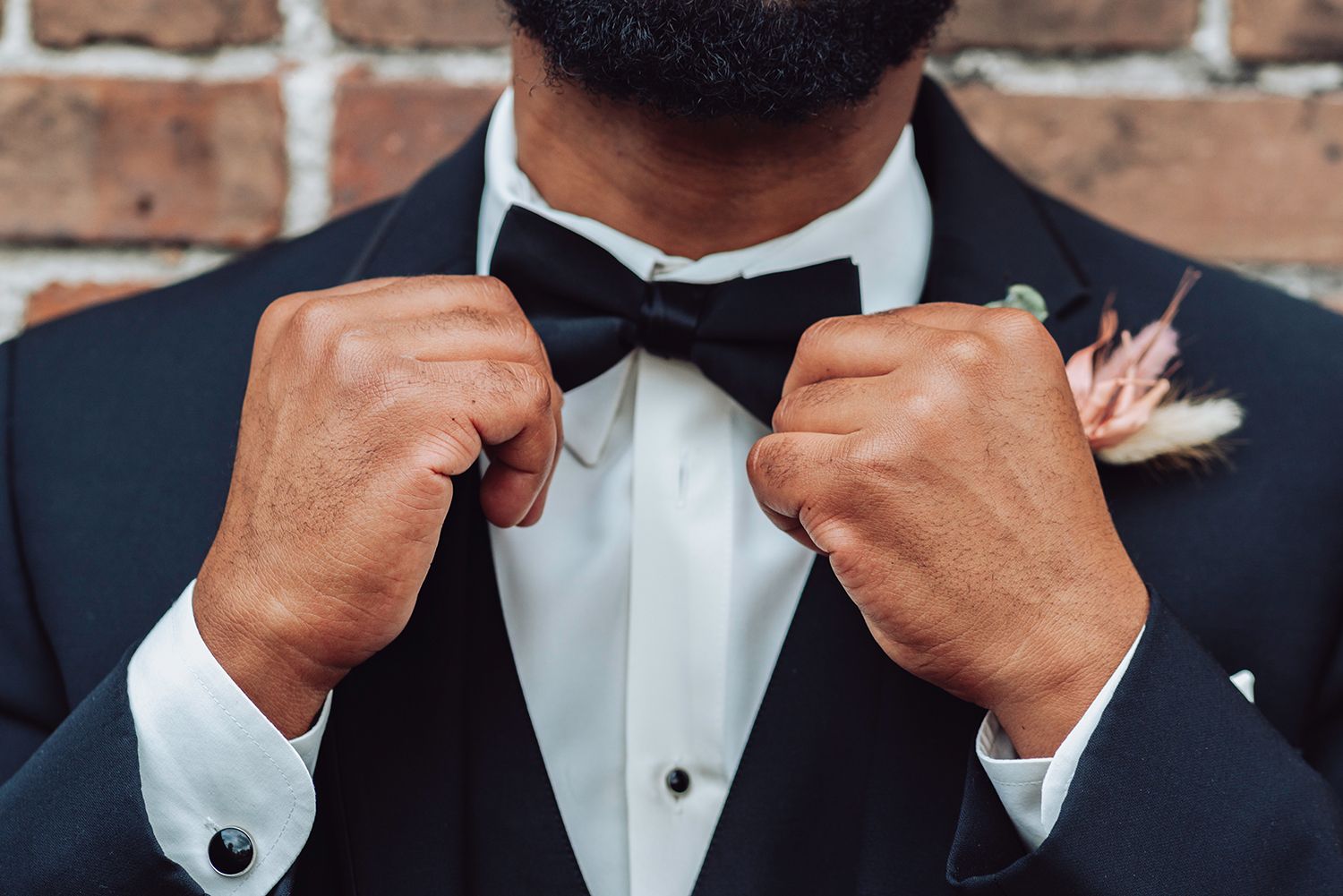 Close-up of hands adjusting a black bowtie on a formal tuxedo with white dress shirt and cufflinks for wedding photographer in Jacksonville.