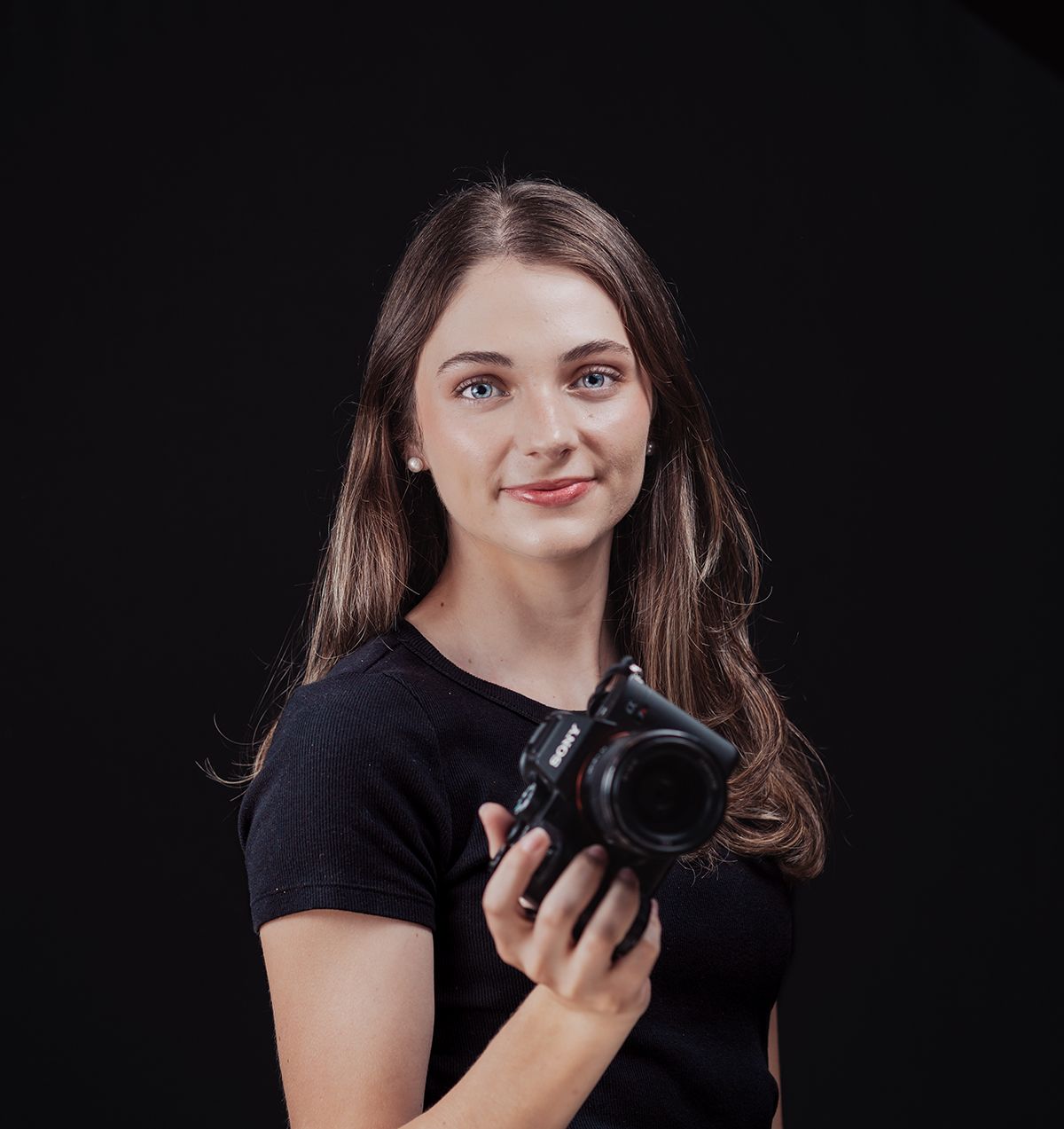 Professional photographer in black t-shirt holding DSLR camera against dark background.
