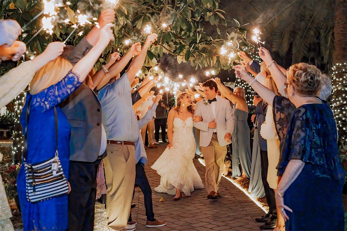 Wedding guests form a sparkler tunnel exit at an outdoor evening reception creating a magical light display.