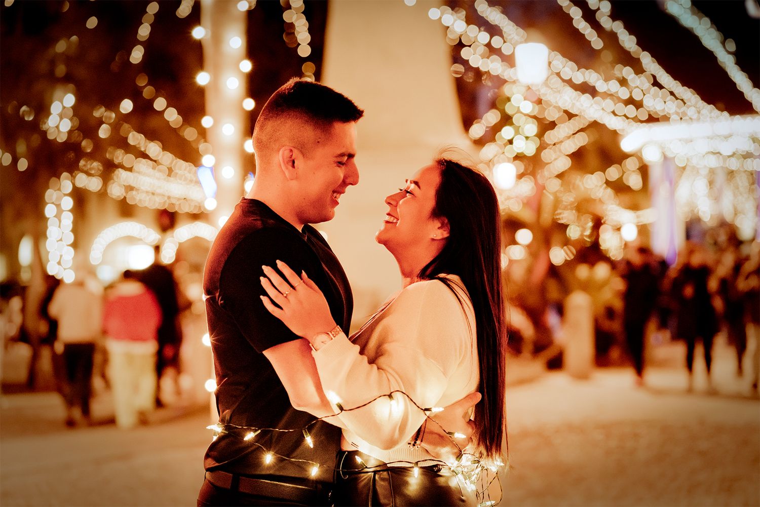 Romantic couple embraces under twinkling string lights during an evening celebration.