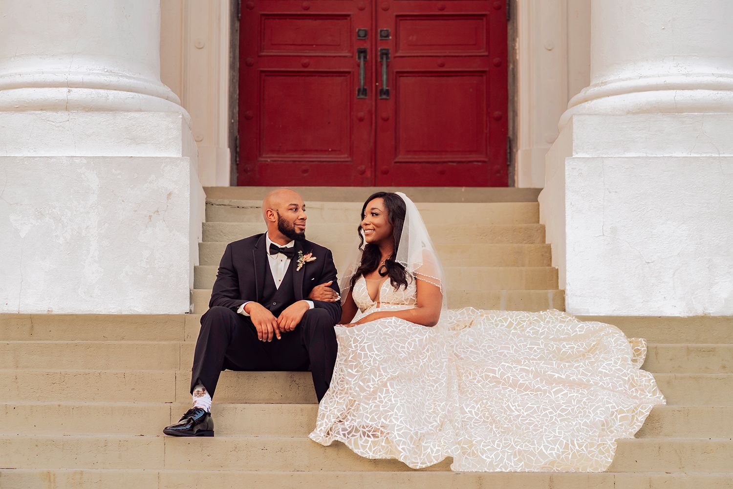 A couple sits together on white stone steps in front of a red door for wedding photographer in Jacksonville, Florida
