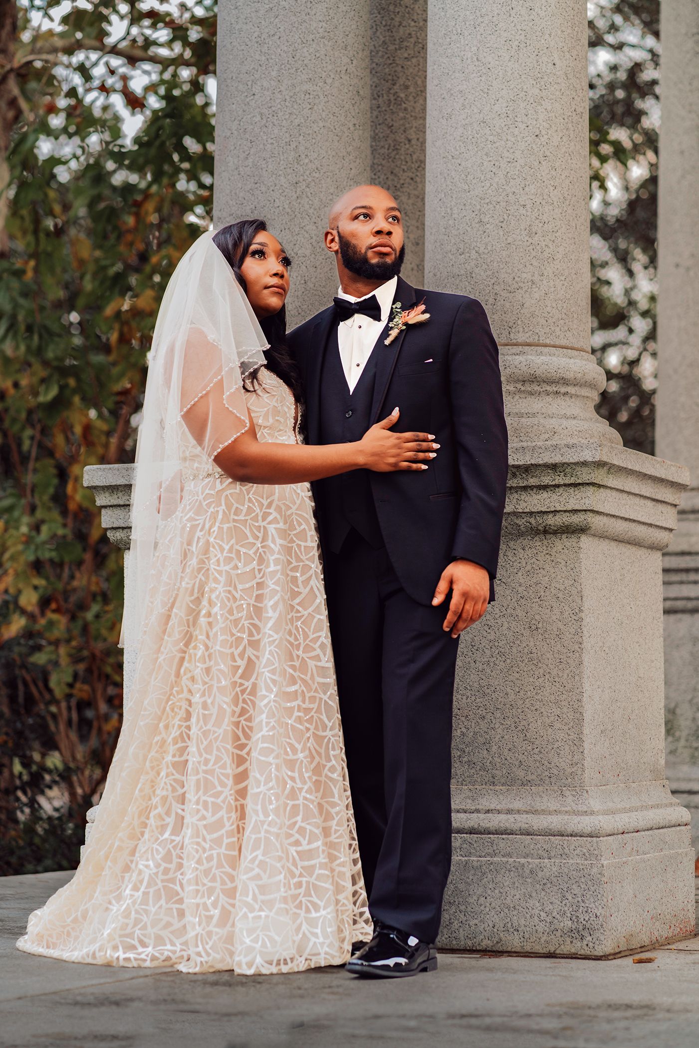 A couple in wedding attire shares a playful moment between stone columns in a romantic outdoor setting in Jacksonville, Florida