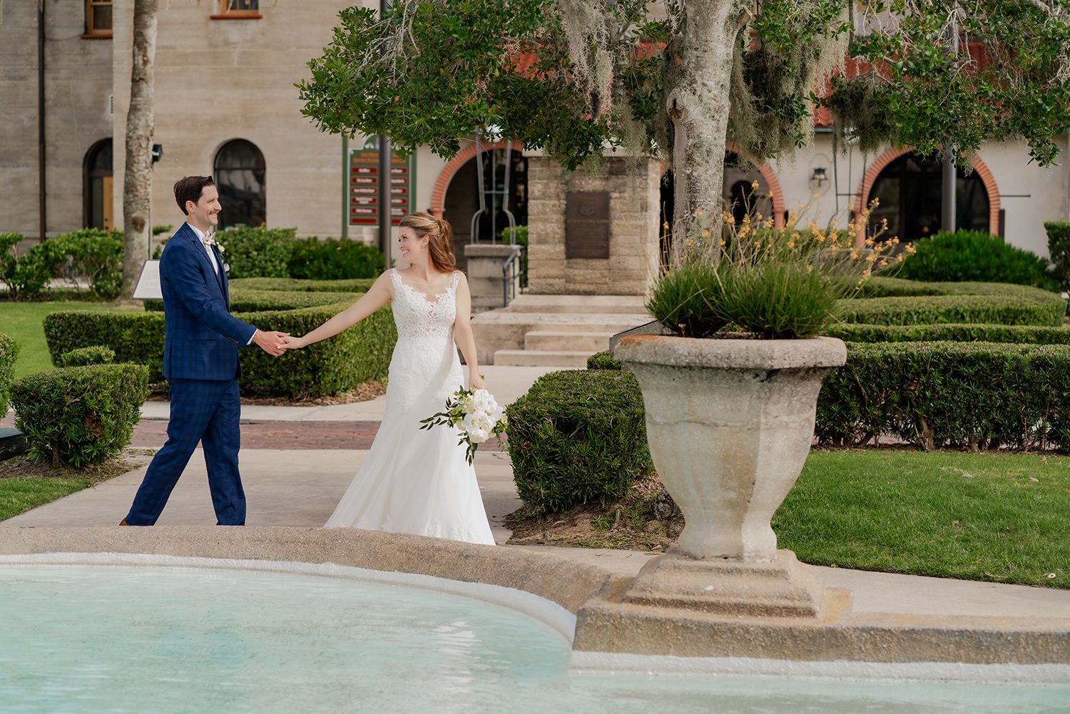 Couple shares a romantic moment in a garden courtyard with Mediterranean-style architecture and lush greenery.
