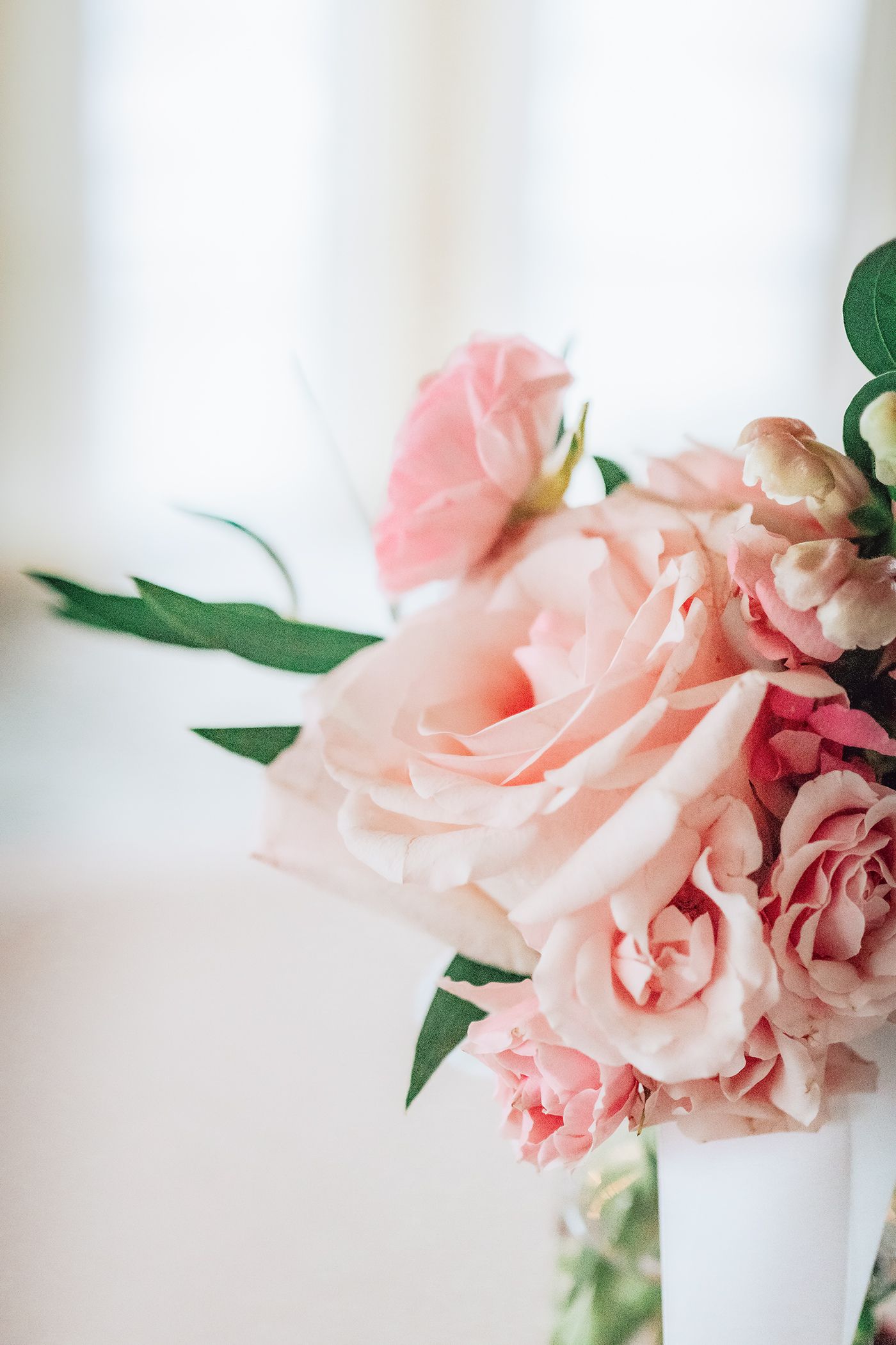 Delicate pink roses with soft petals arranged in a white vase against a light background.