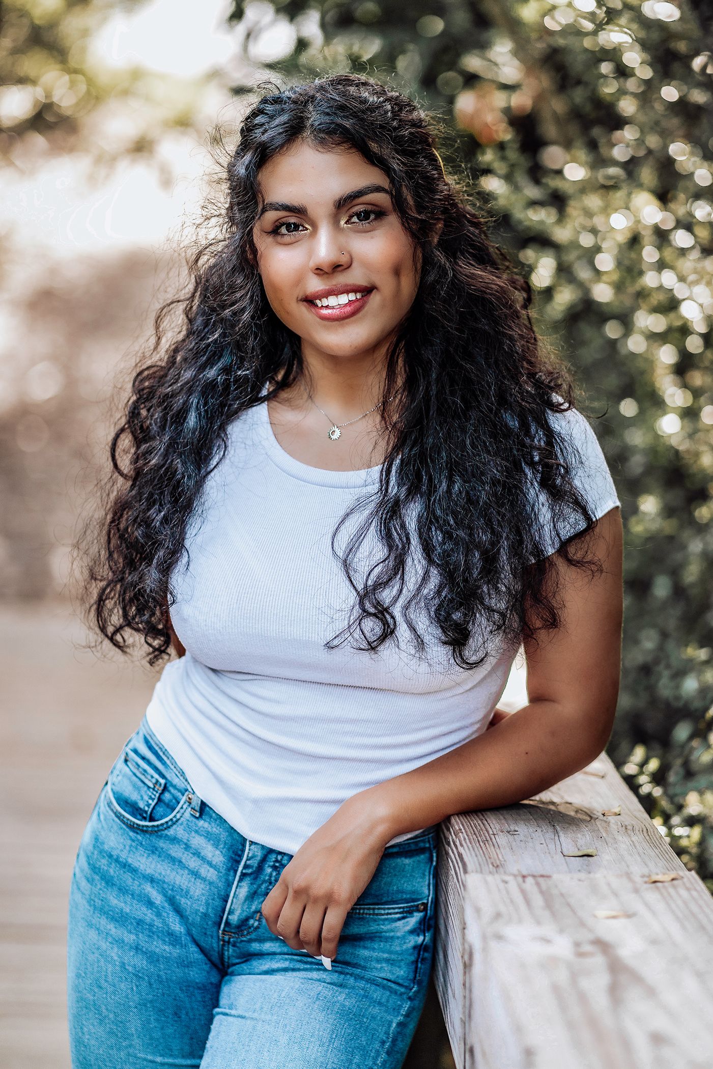High school senior in a white t-shirt and blue jeans poses against a light colored wall with greenery in Jacksonville, Florida