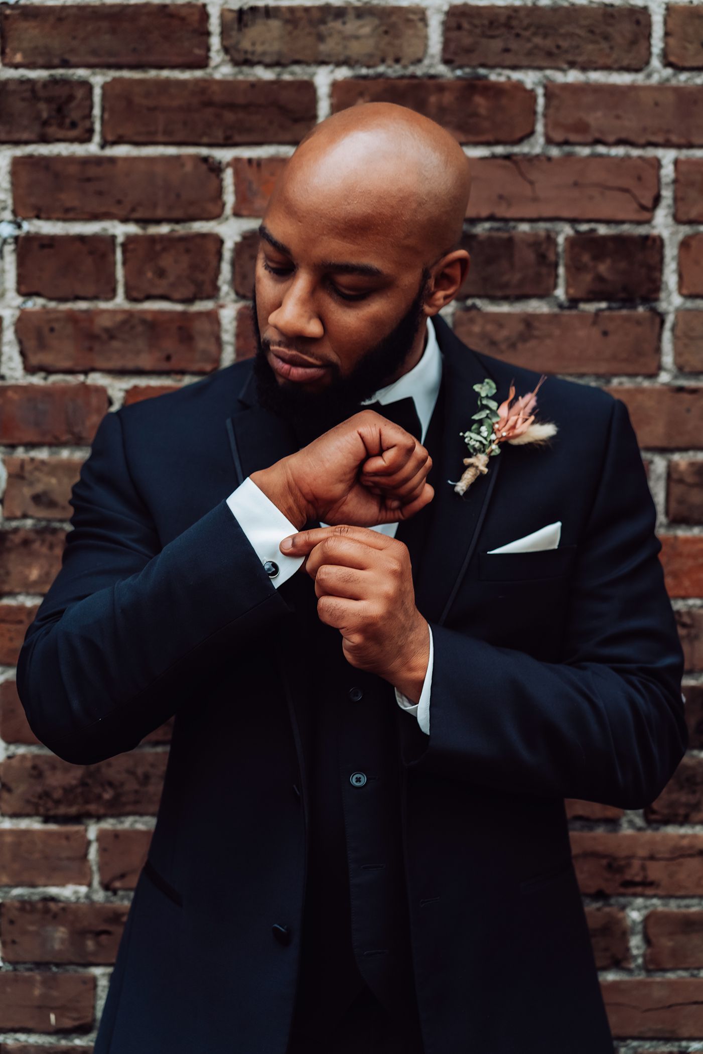 A groom in a black suit and boutonniere adjusts cuffs while preparing for wedding in Jacksonville, Florida.