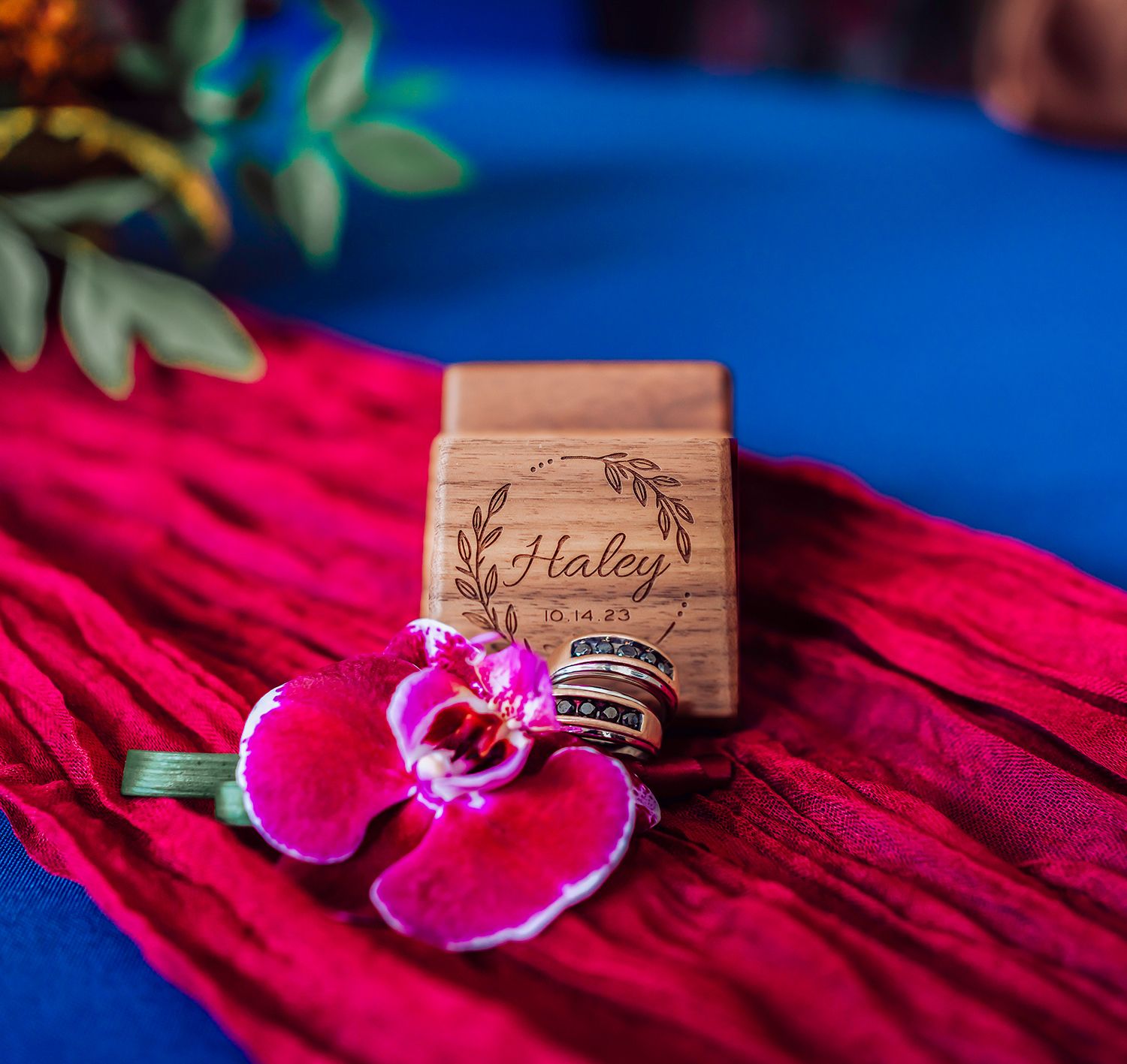 Wedding rings rest on a bright pink flower petal against a vibrant blue background.