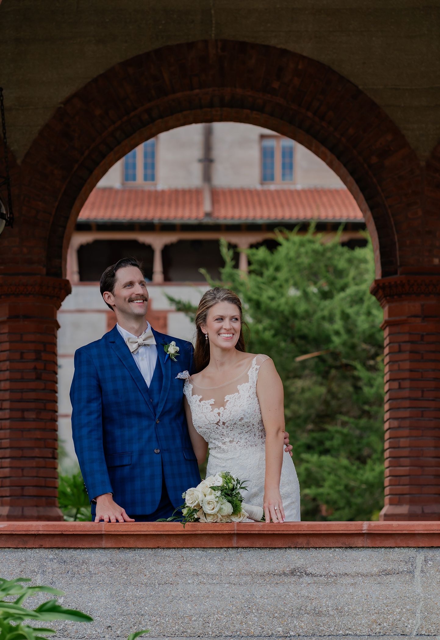 A couple poses together under brick archways at an outdoor venue on their wedding day.