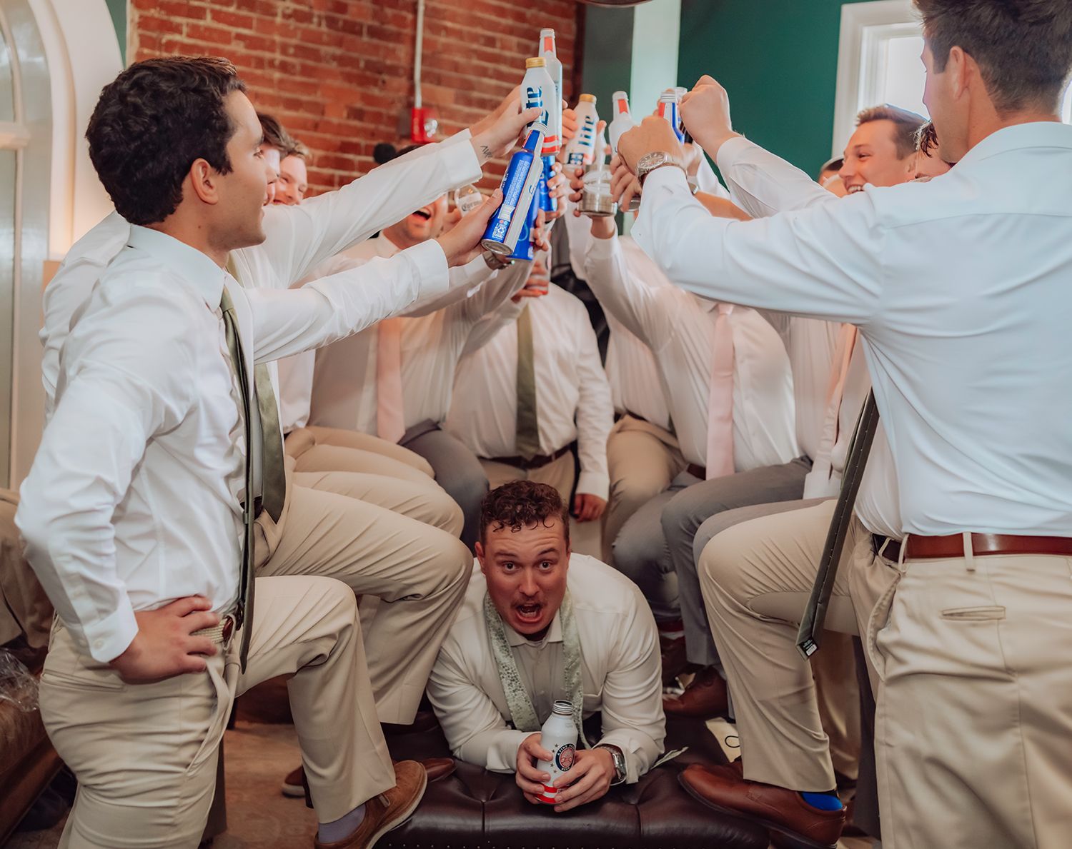 Groomsmen in khaki pants and white shirts celebrate and dance at a wedding reception.
