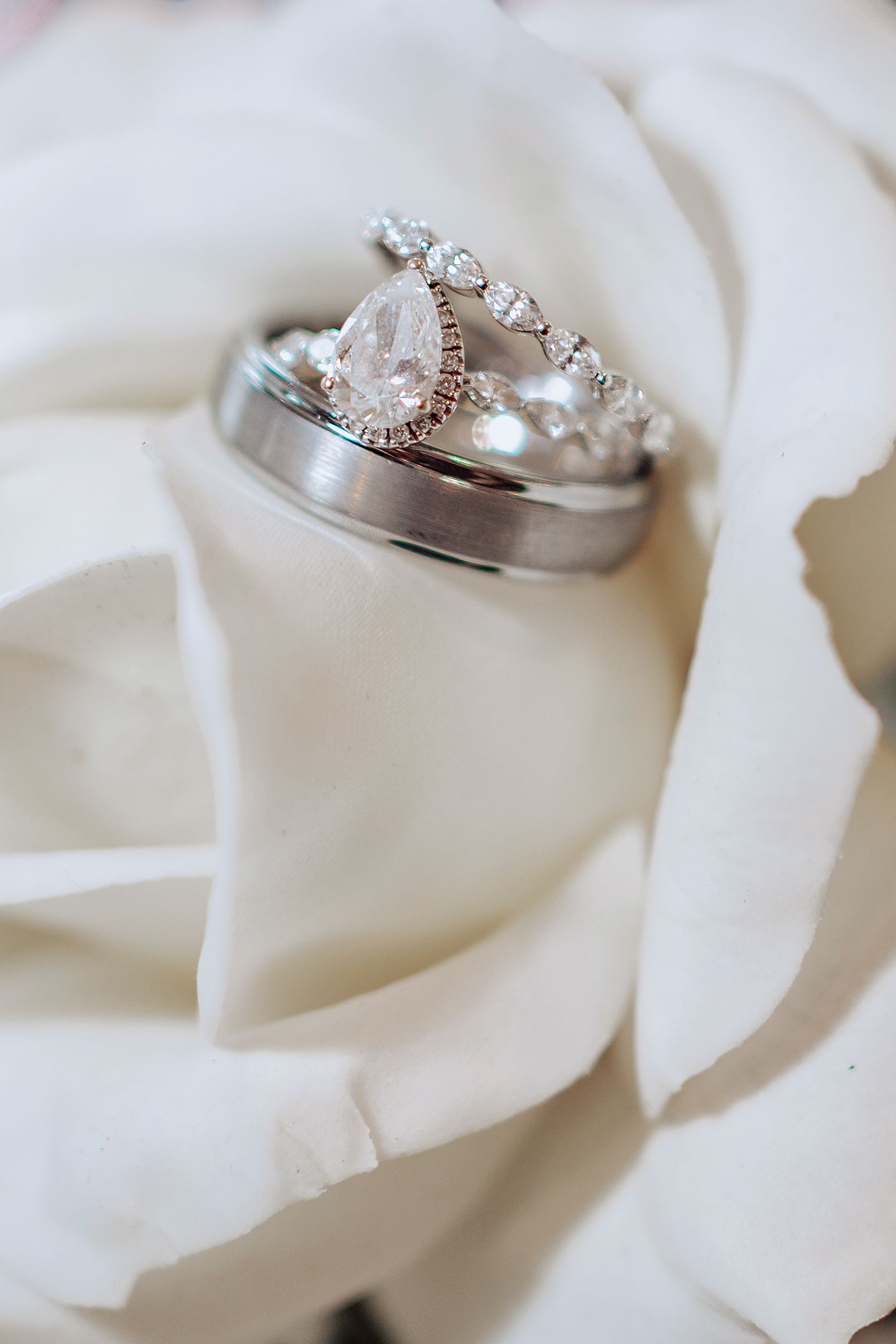 Elegant diamond engagement ring nestled in soft white rose petals creating a romantic wedding detail shot.