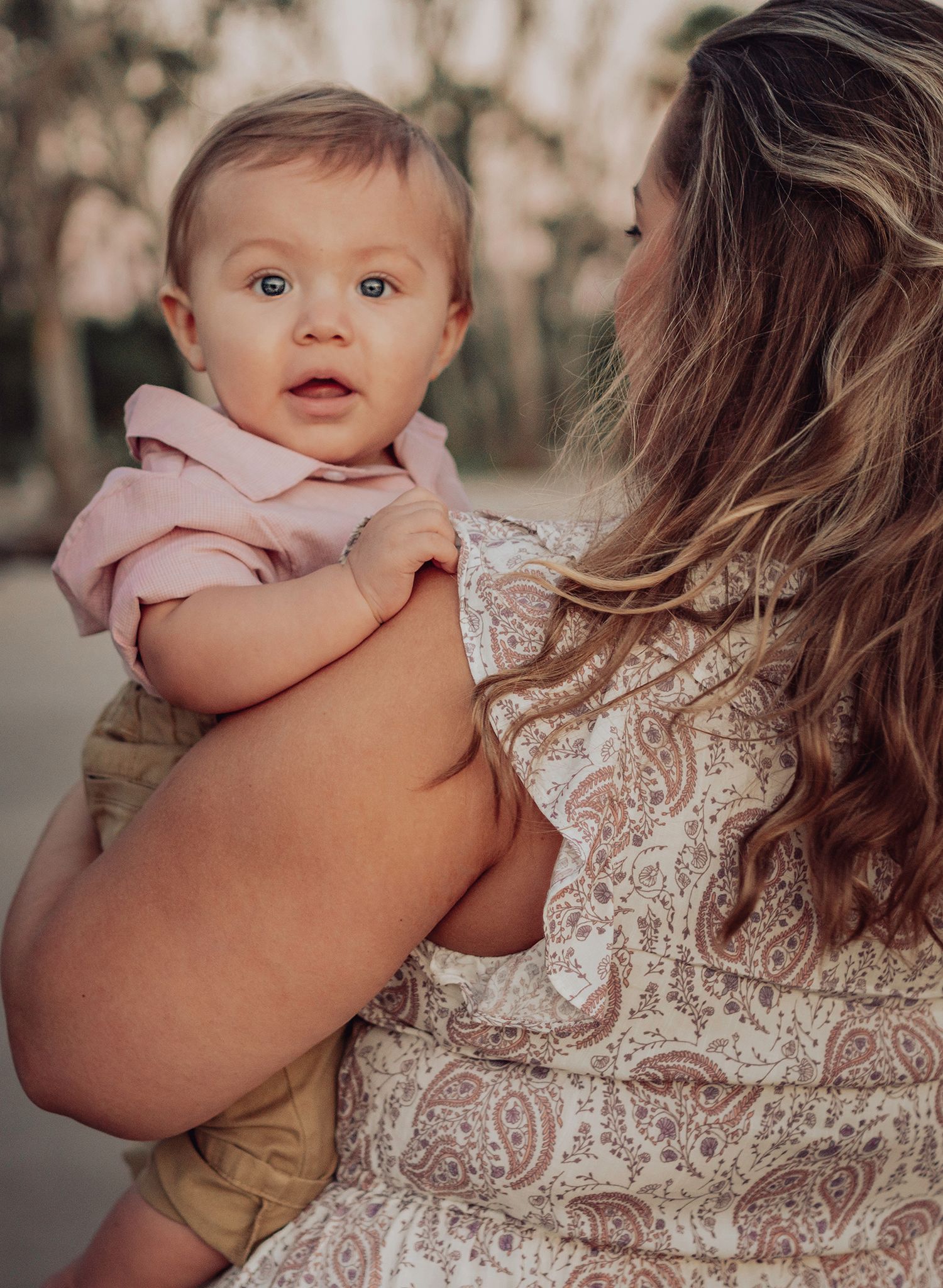 A baby in pink clothing rests against someone wearing a delicate lace dress in an outdoor setting in Jacksonville, Florida