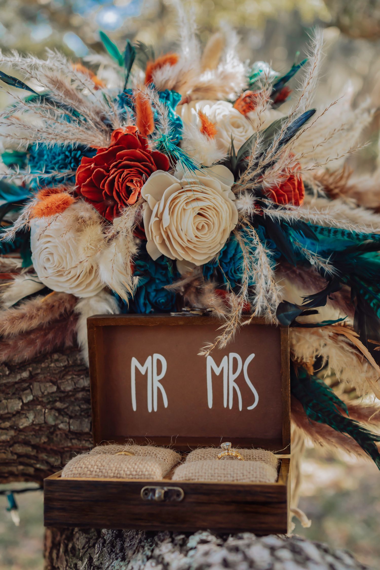 Rustic wooden signs with 'Mr & Mrs' text decorated with cream and red roses and teal foliage at a wedding ceremony.