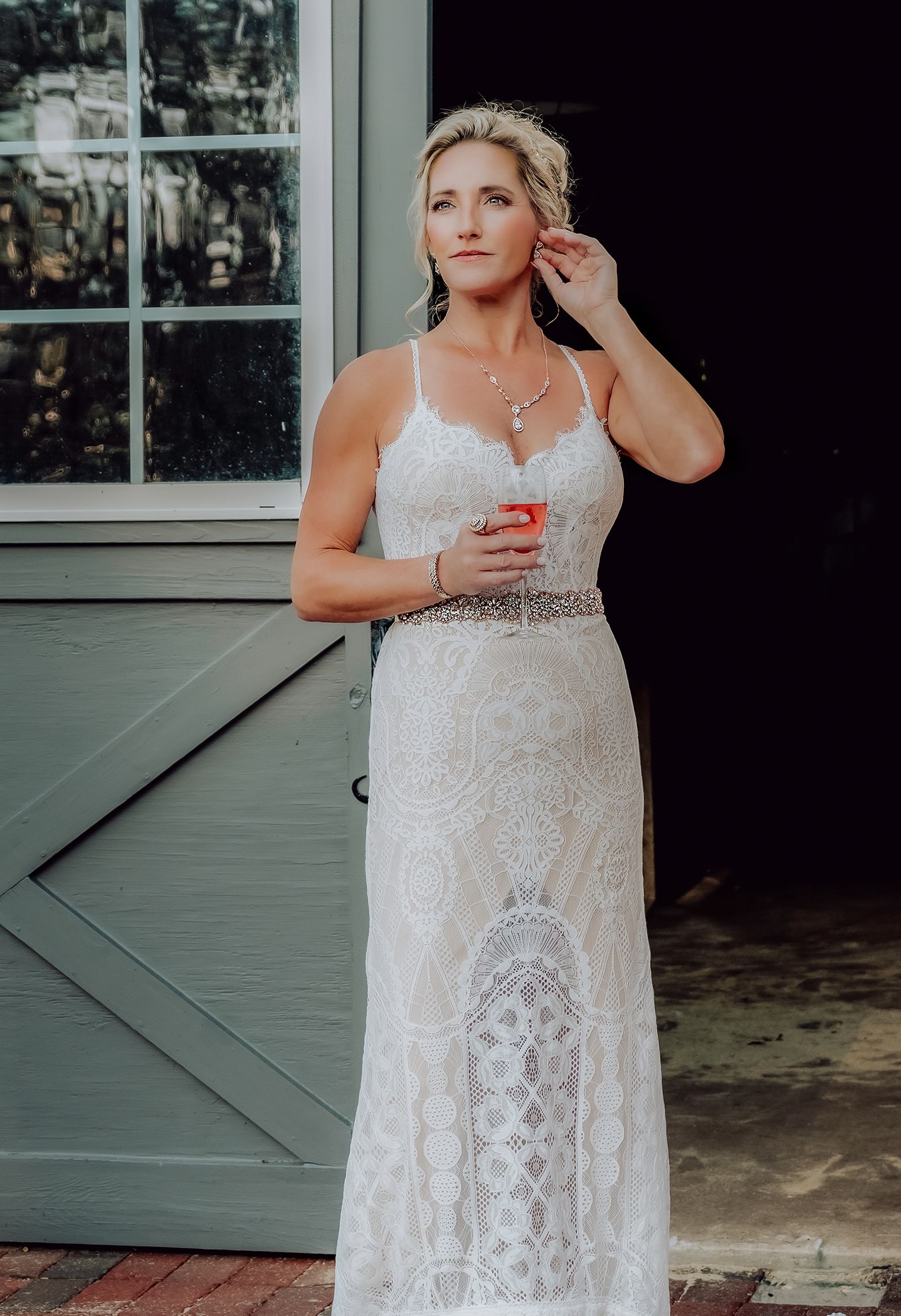 Elegant white lace wedding gown with intricate pattern details and spaghetti straps shown against a green barn door background.