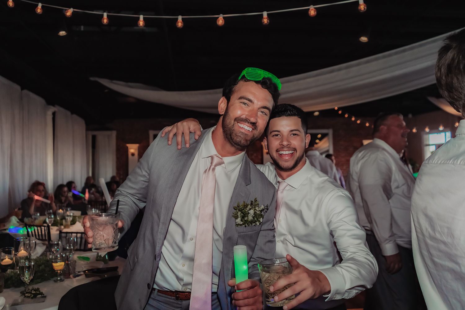 Wedding guests dancing and celebrating under string lights at an outdoor reception party.