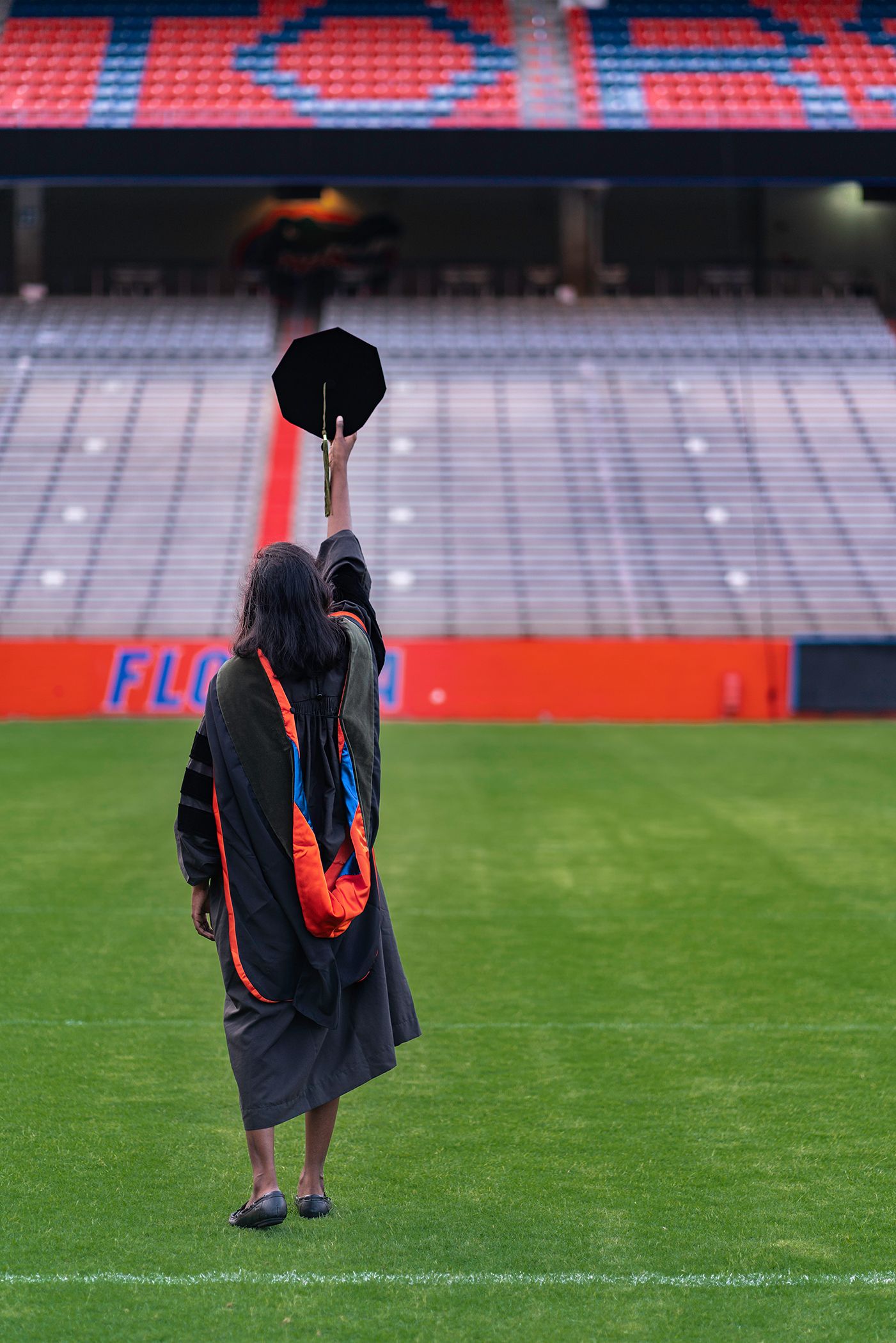 A graduate in academic regalia walks across a football field for graduation photos in Gainesville, Florida at University of Florida