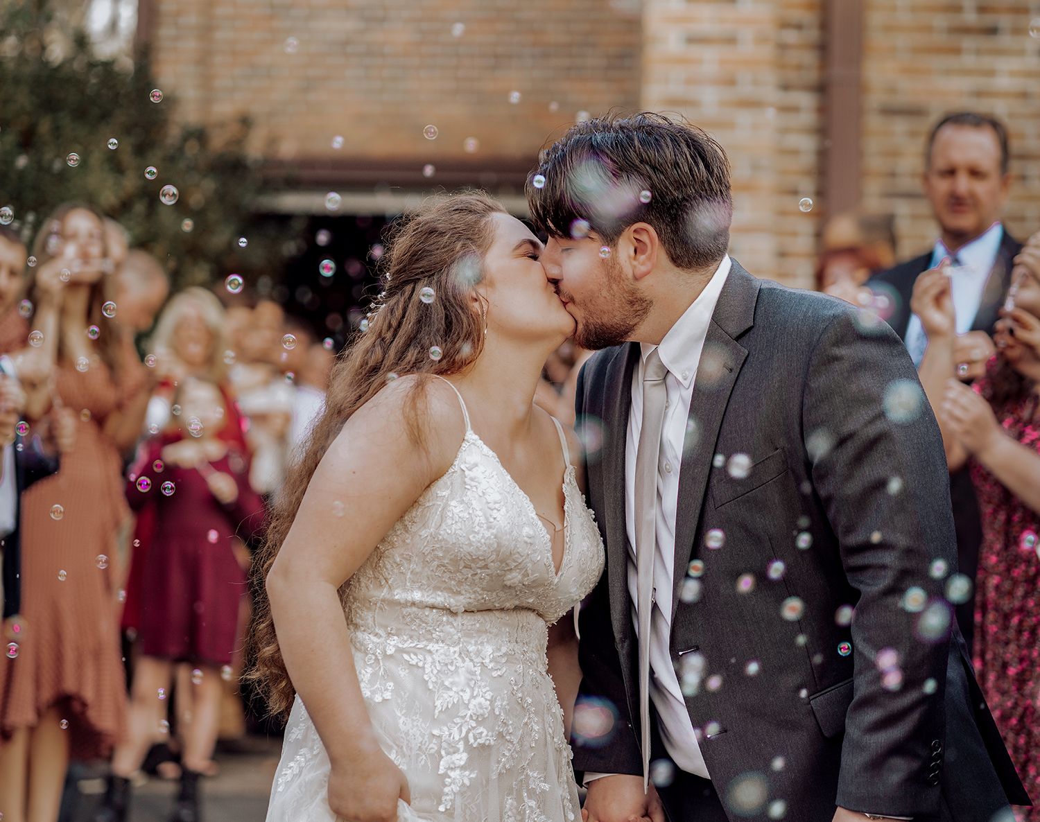 A couple shares a romantic kiss while confetti falls around them at an outdoor wedding ceremony.