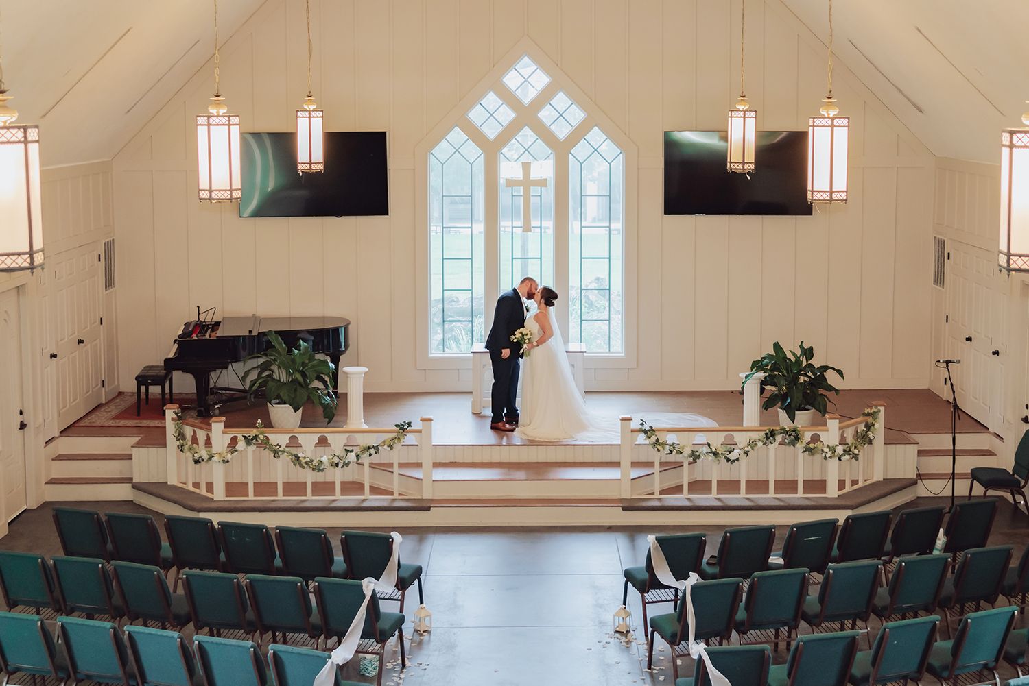 A modern church sanctuary with rows of blue chairs and large windows illuminating the white interior space.