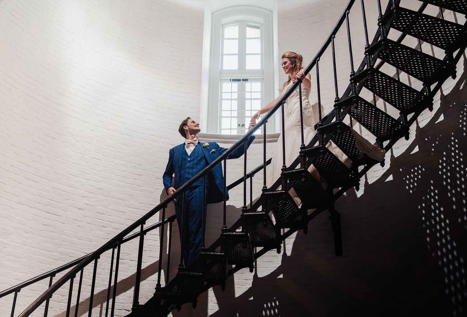 Wedding party members descend a vintage spiral staircase in formal attire.