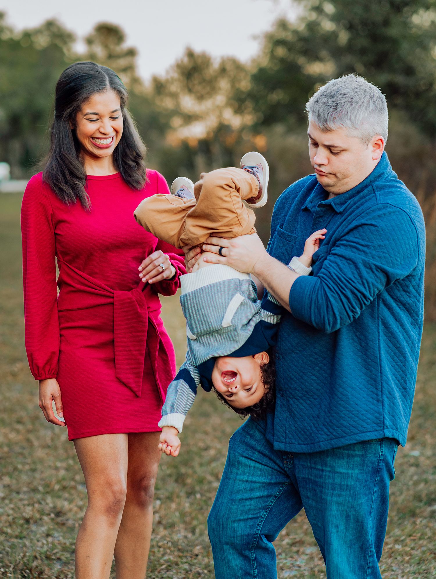 A couple in red and blue outfits plays with a small child outdoors during a candid family photoshoot in Gainesville Florida