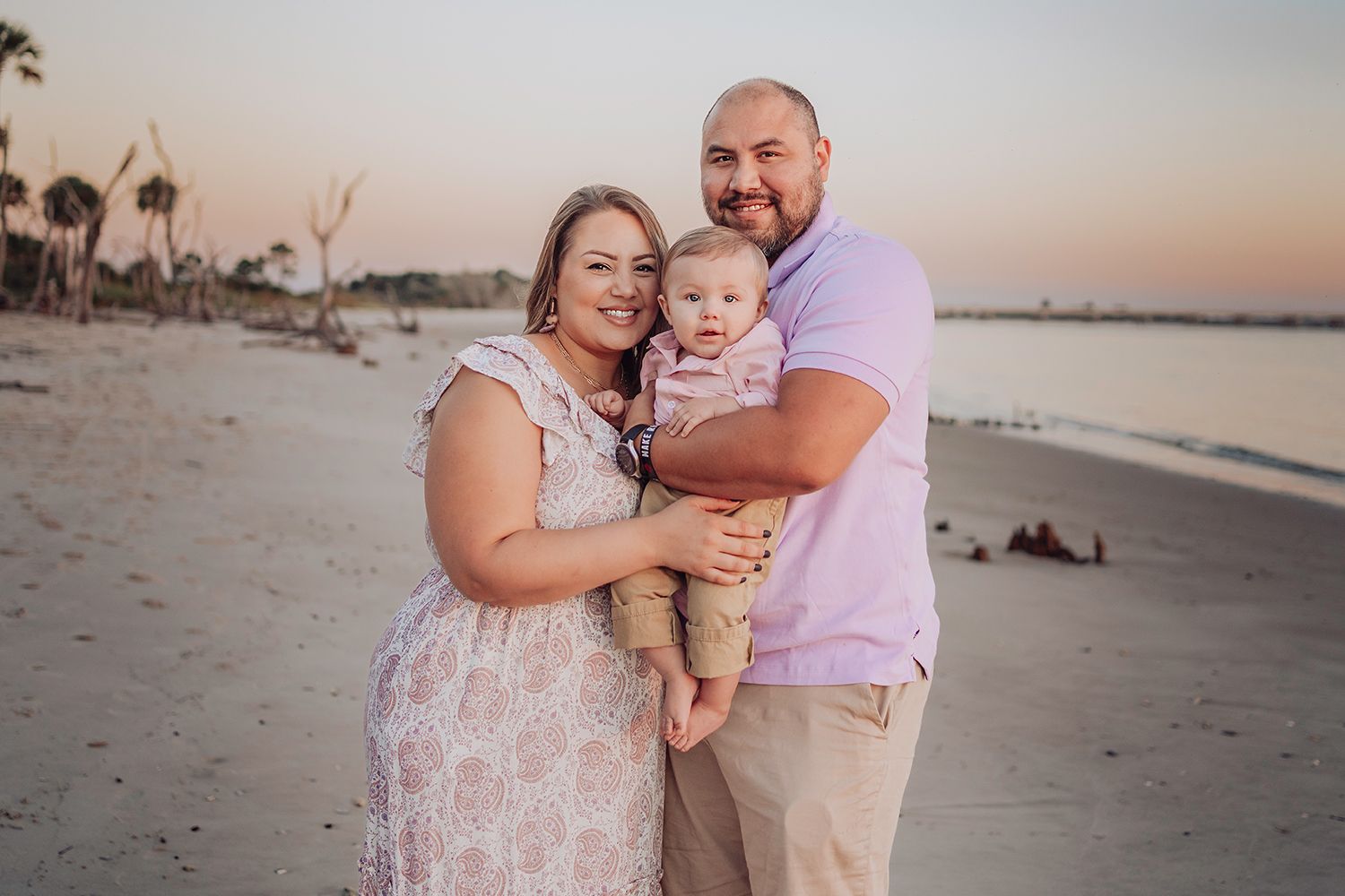 A family in coordinated pink and beige outfits shares tender moments together on a beach at sunrise in Jacksonville Florida