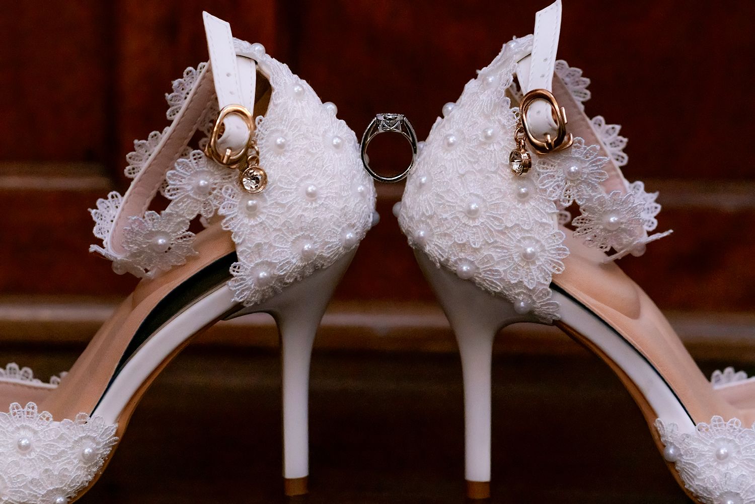 White bridal shoes adorned with delicate lace and pearl embellishments displayed in various angles on a wooden surface.