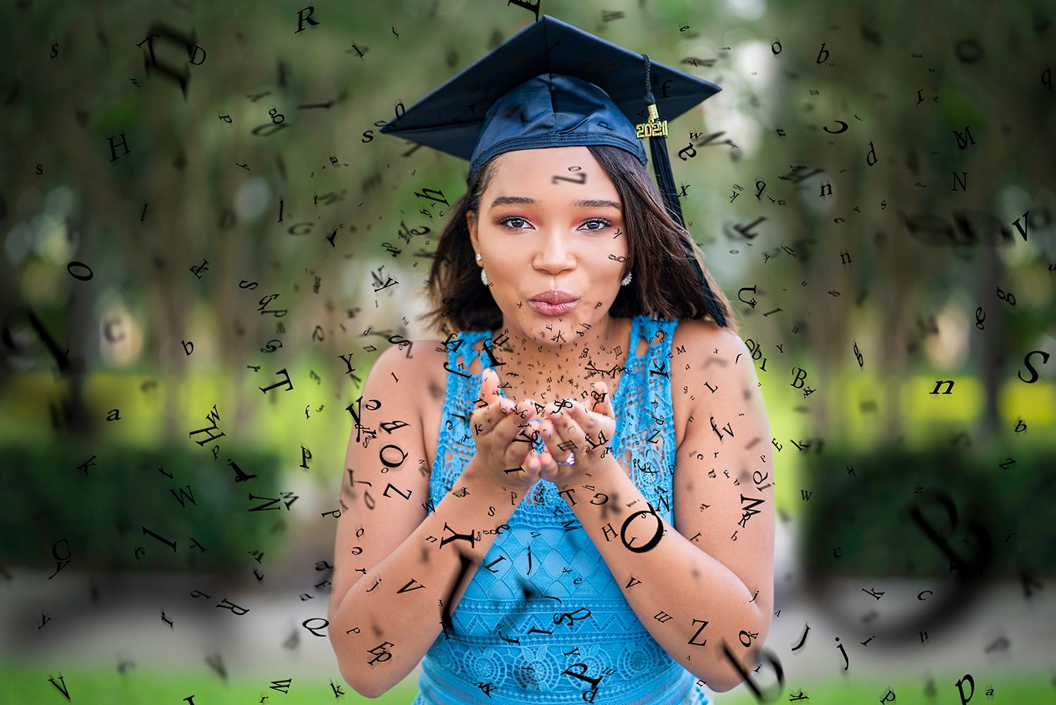 Graduate in blue cap and gown poses with hands up showing peace signs during outdoor graduation photoshoot.