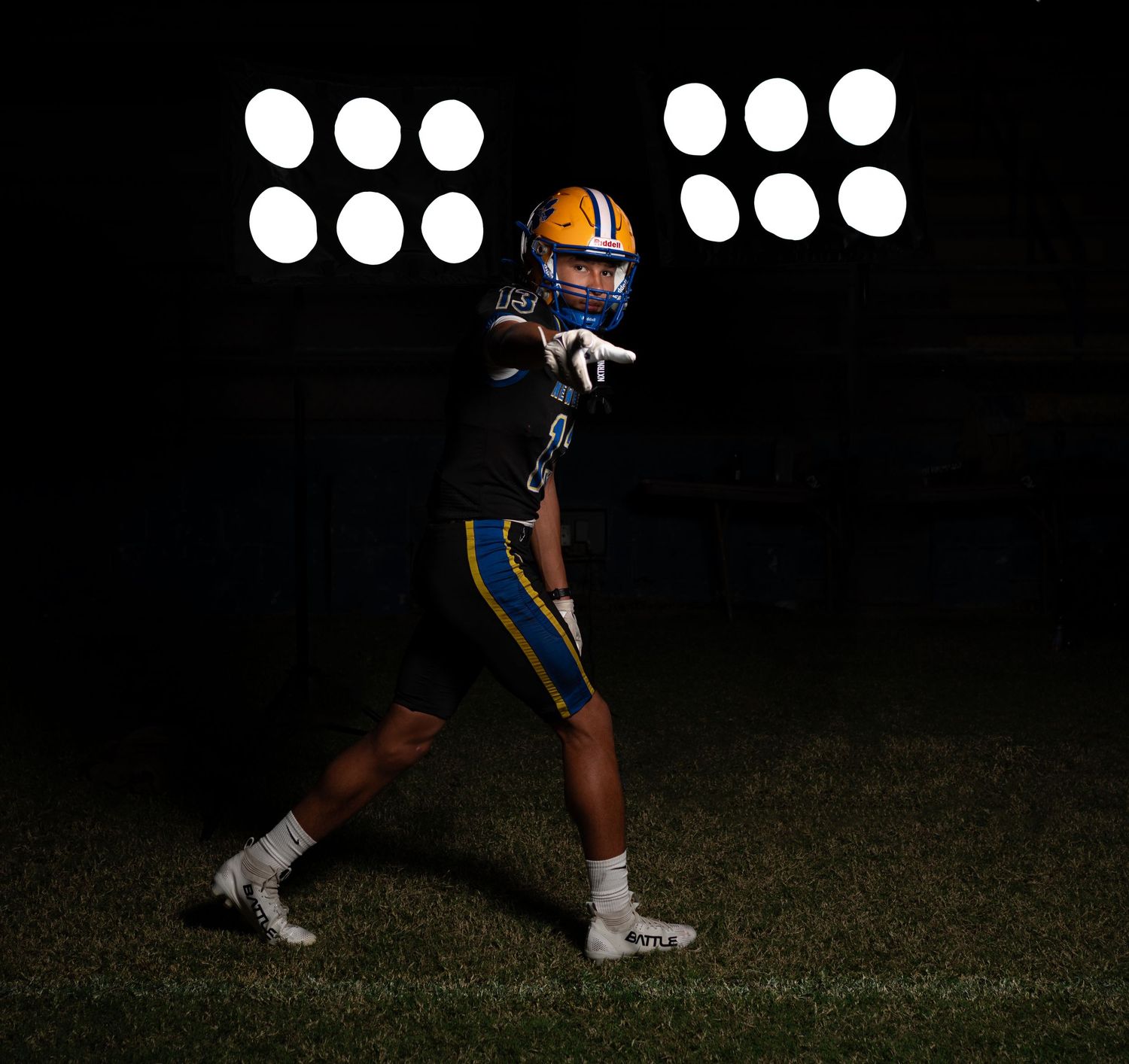 Football player in blue and gold uniform and orange helmet poses under stadium lights at night.