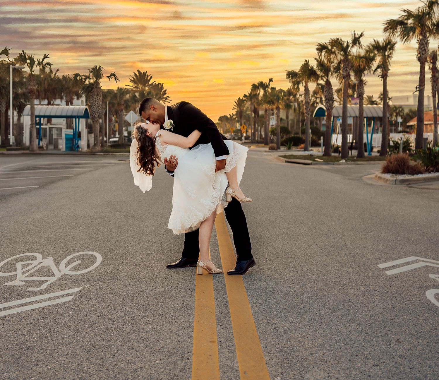 A romantic couple dips and embraces on a palm tree-lined street during a golden sunset for wedding photographer in Vilano Beach