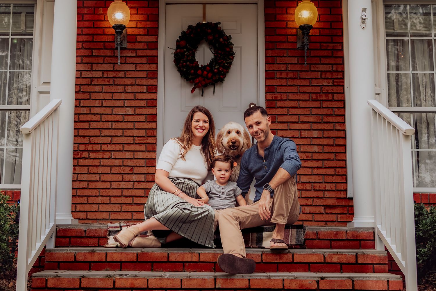 A family and their dog sit together on the front steps of a red brick house with white trim for family photos in Gainesville, Florida