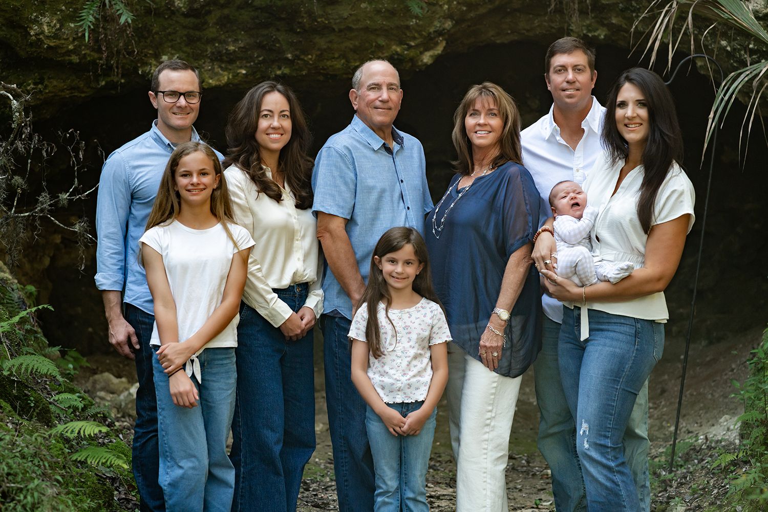 A group of people wearing coordinated blue and white outfits pose together outdoors in a natural setting for family photographer in Ocala