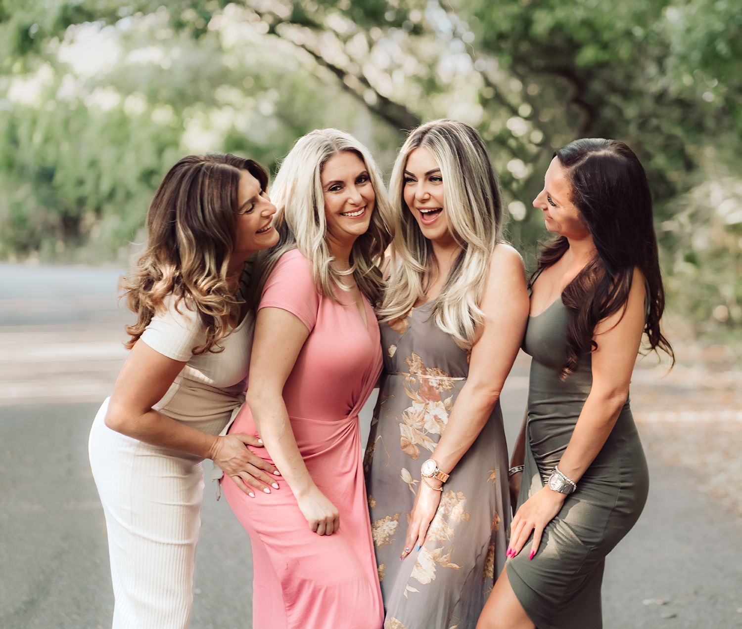 Adult sisters in fitted dresses laugh together while posing on a paved road with greenery for family photos in Jacksonville, Florida