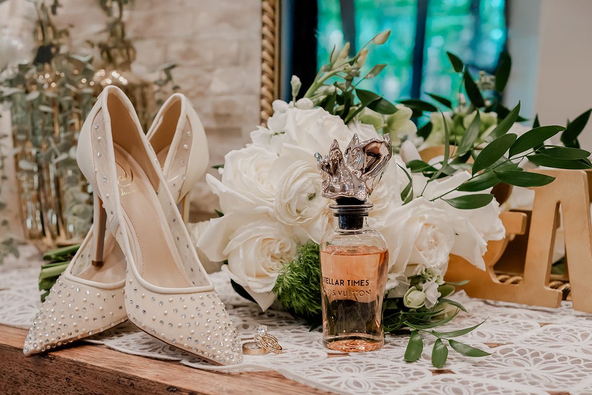 Elegant wedding details including lace, perfume bottles, and delicate floral arrangements displayed on a white tablecloth.