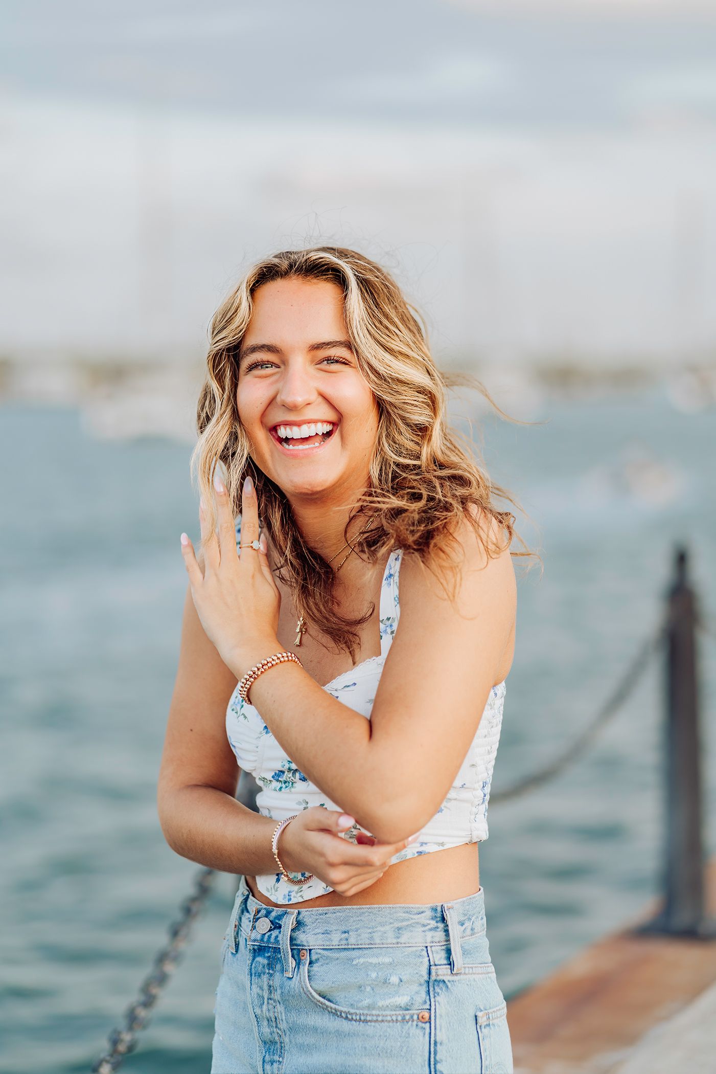 A high school senior in denim shorts and white top poses by the water on a sunny day in St. Augustine, Florida for graduation photos.