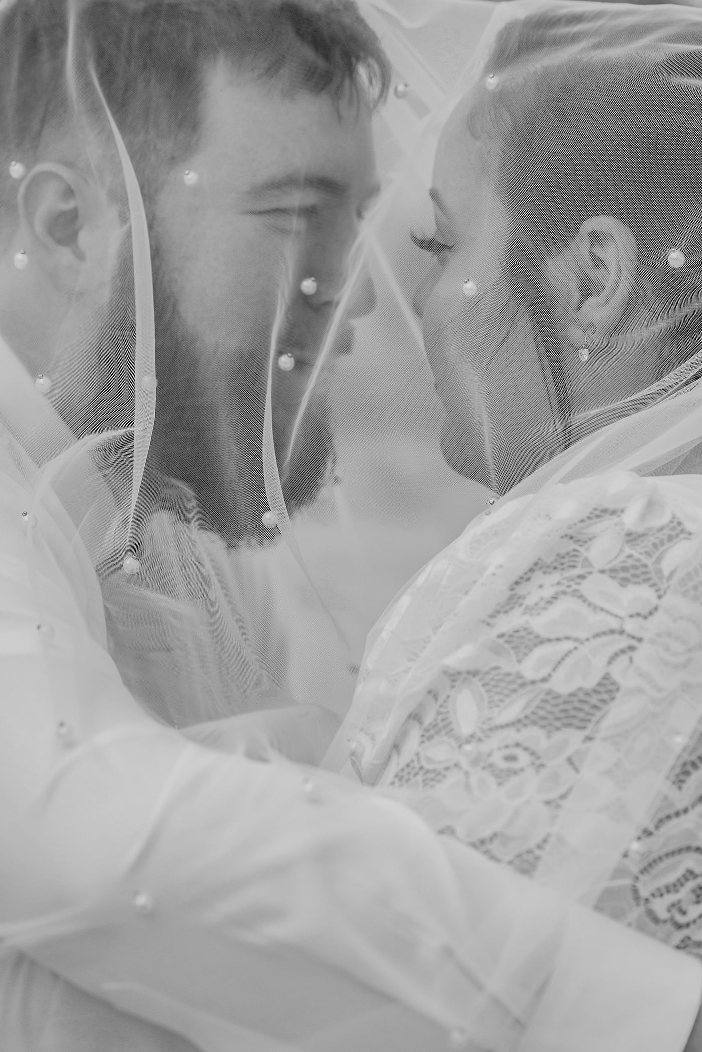 A romantic black and white wedding photo series showing a couple kissing under a delicate veil.