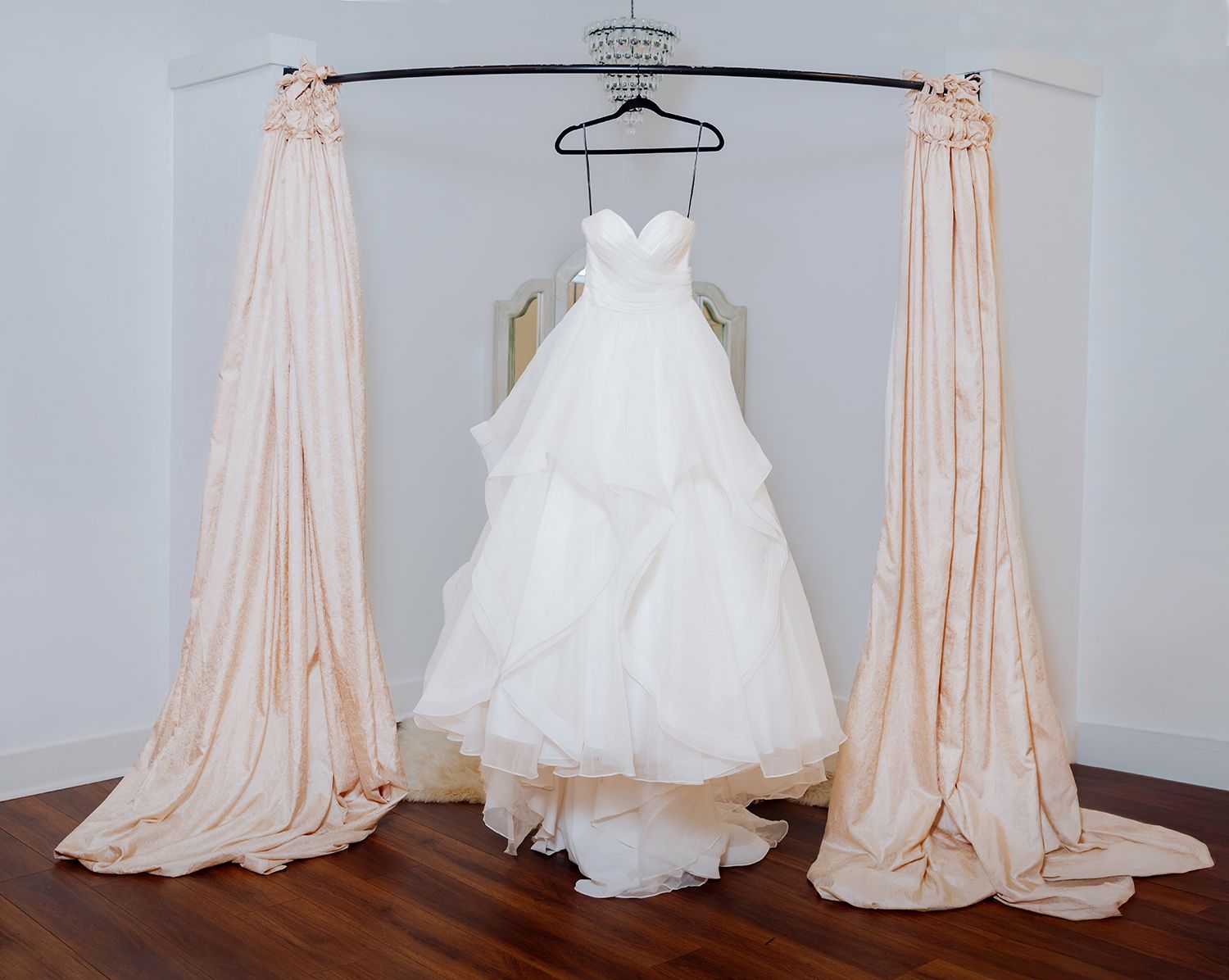 A white wedding dress and blush pink bridesmaid dress displayed side by side on hangers against a gray wall.