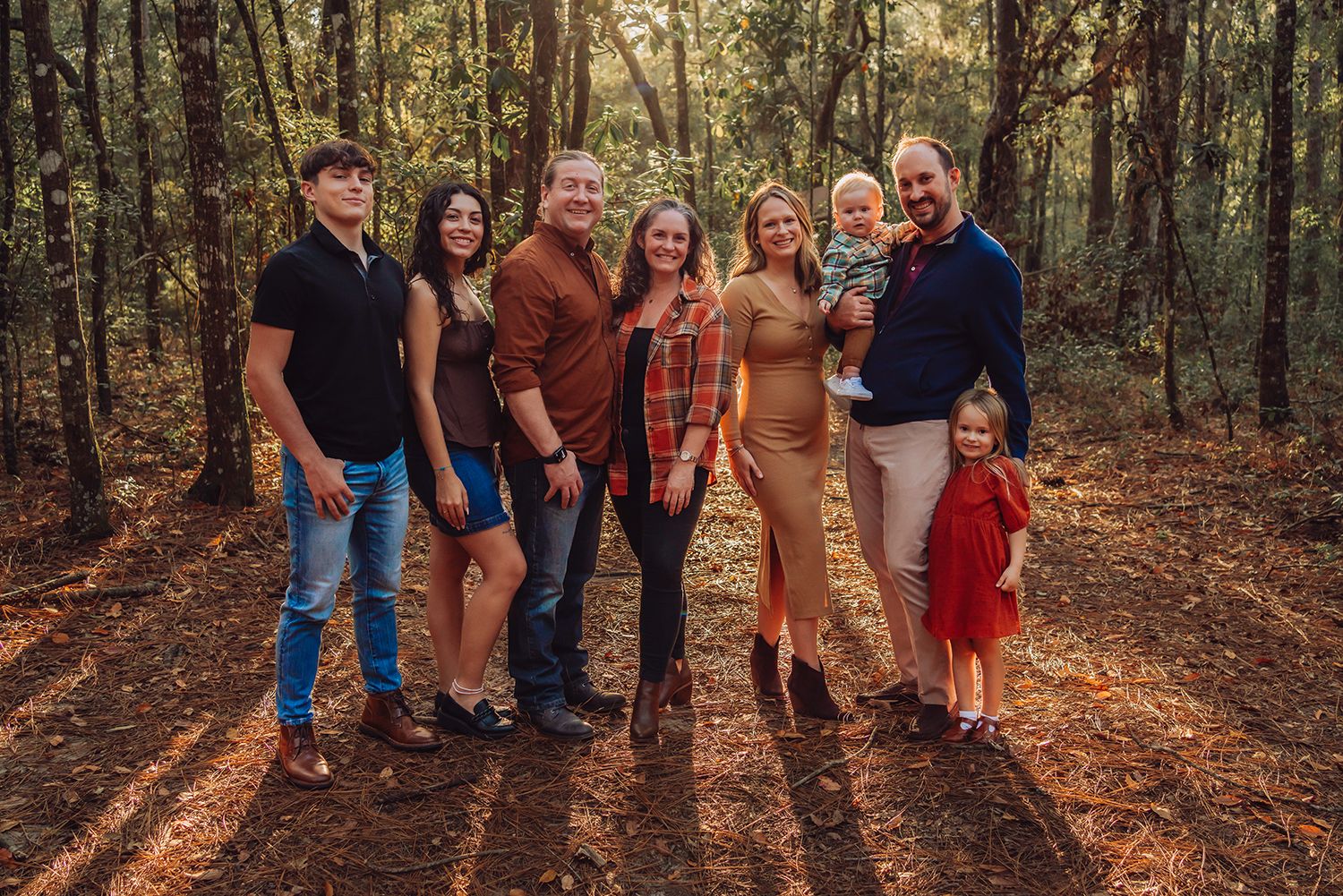 Family walking together on a forest trail covered in autumn leaves during golden hour for family photos in Gainesville Florida