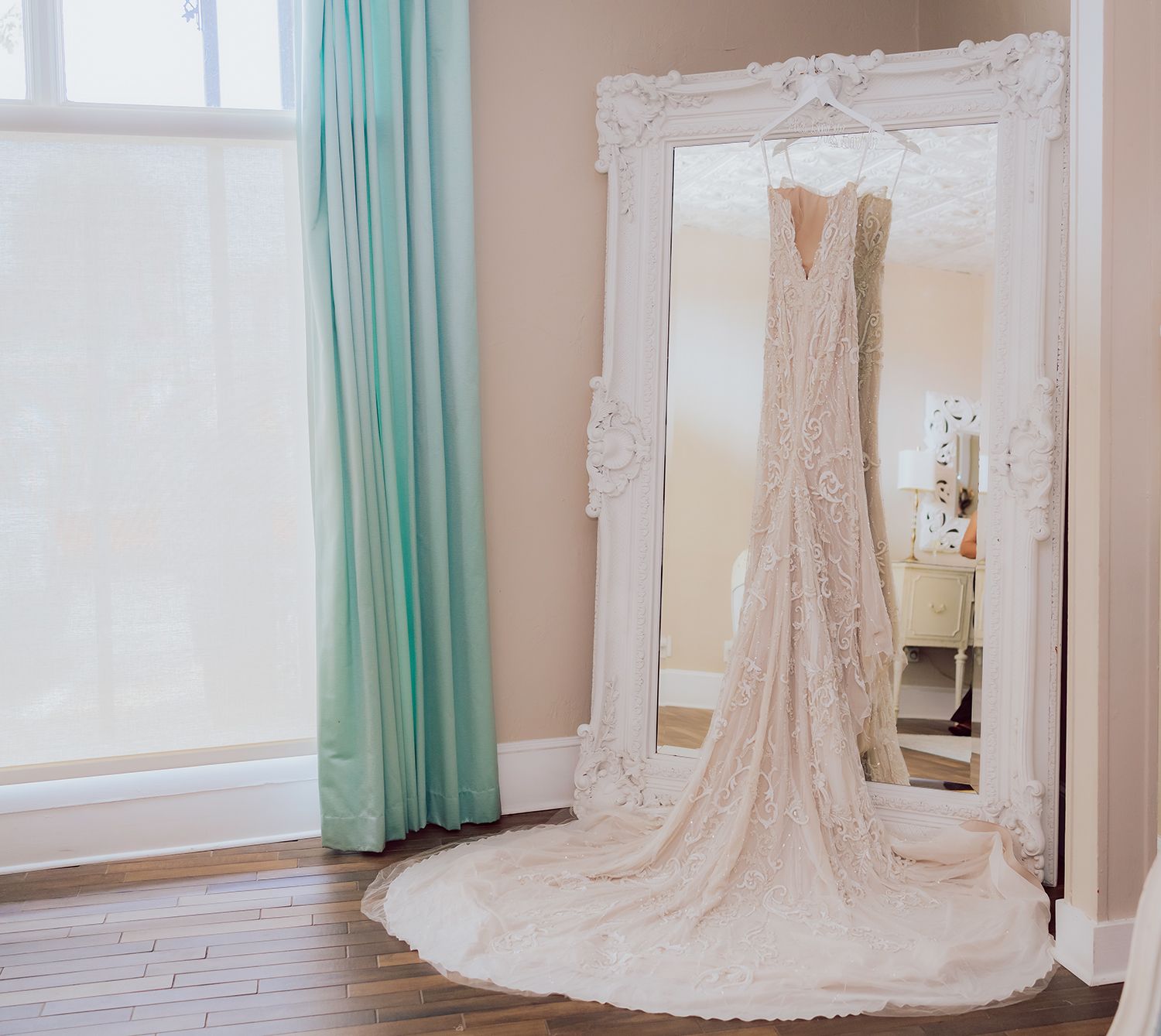 A bridal boutique interior with turquoise curtains and ornate white mirrors displays elegant wedding gowns.