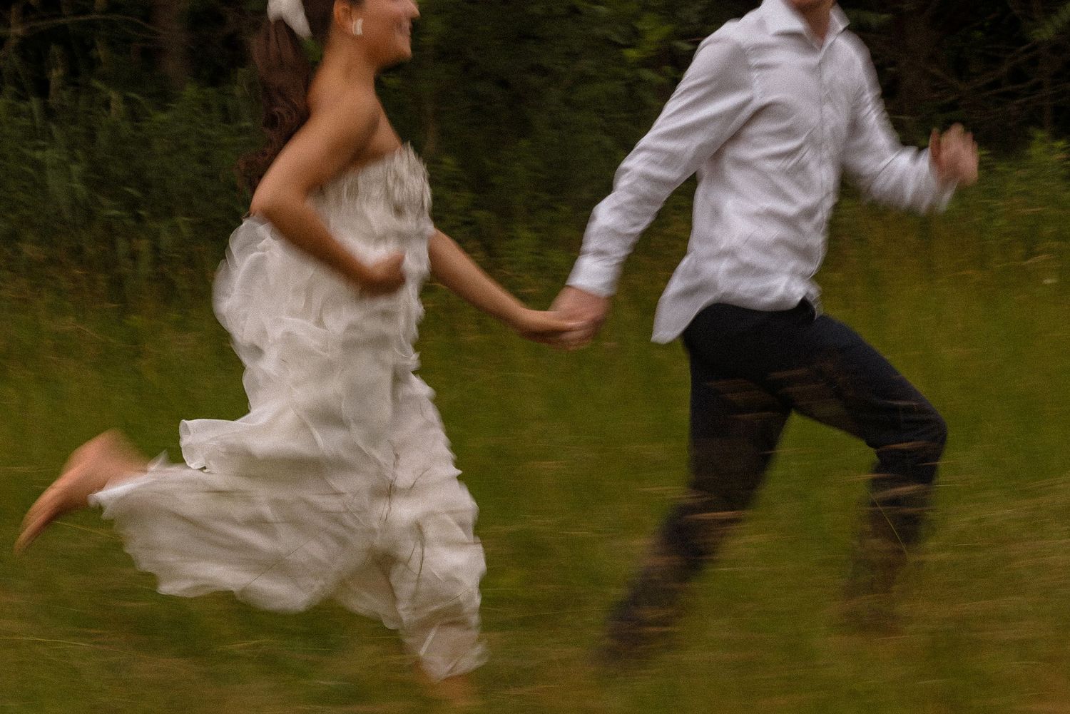 Wedding couple performing energetic dance moves on an outdoor lawn.