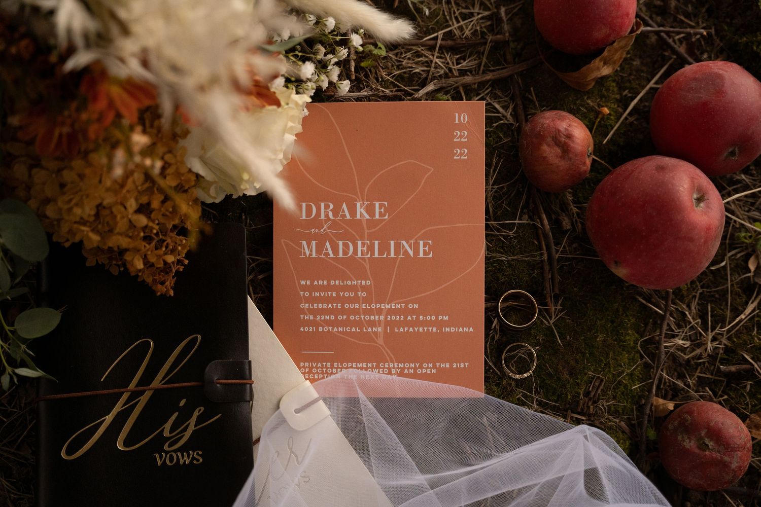 Wedding stationery and red apples arranged artistically on a dark surface.