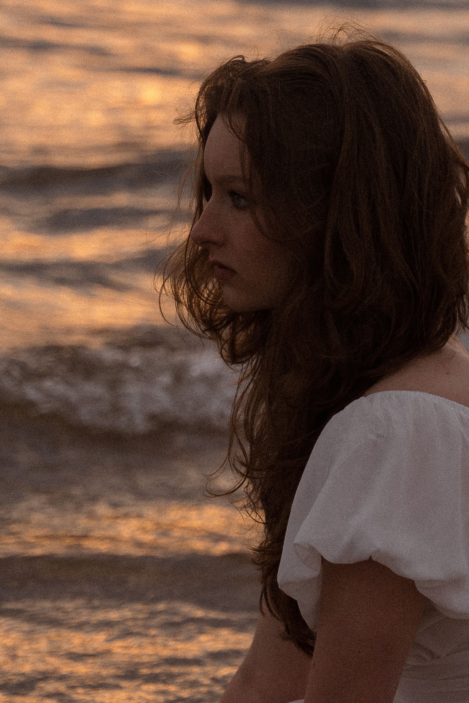 Romantic seaside portrait with windswept hair against a golden sunset over the ocean.