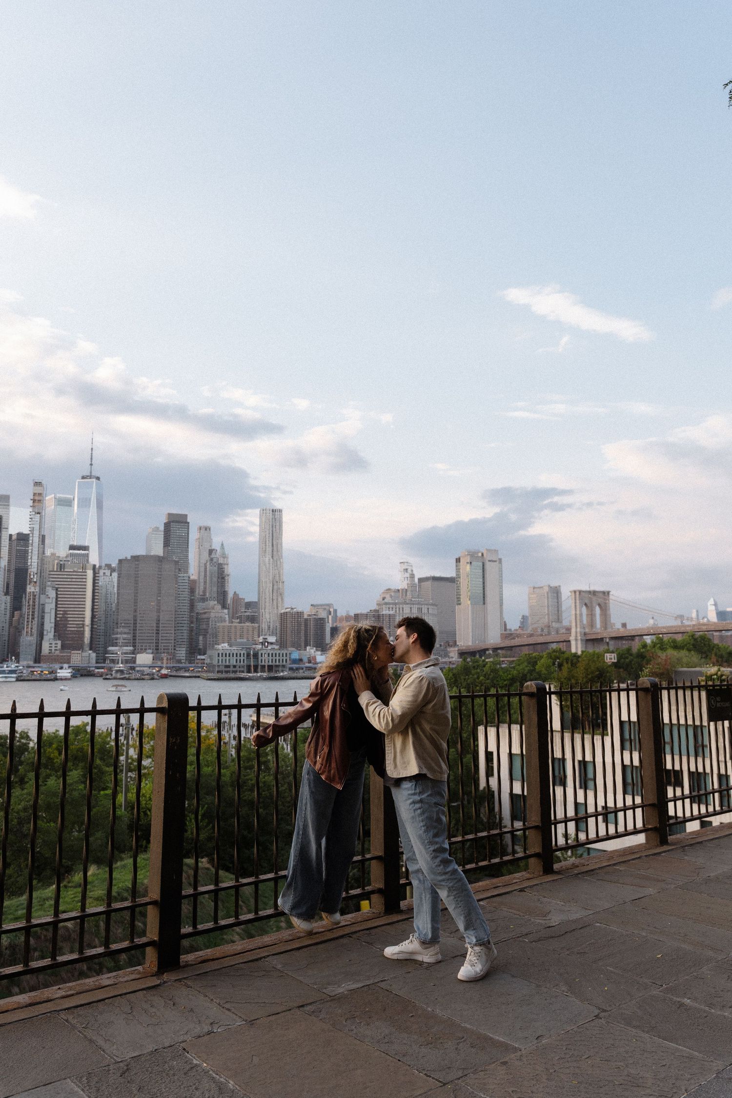 Romantic couple sharing a tender moment at a scenic viewpoint overlooking the Manhattan skyline at sunset.