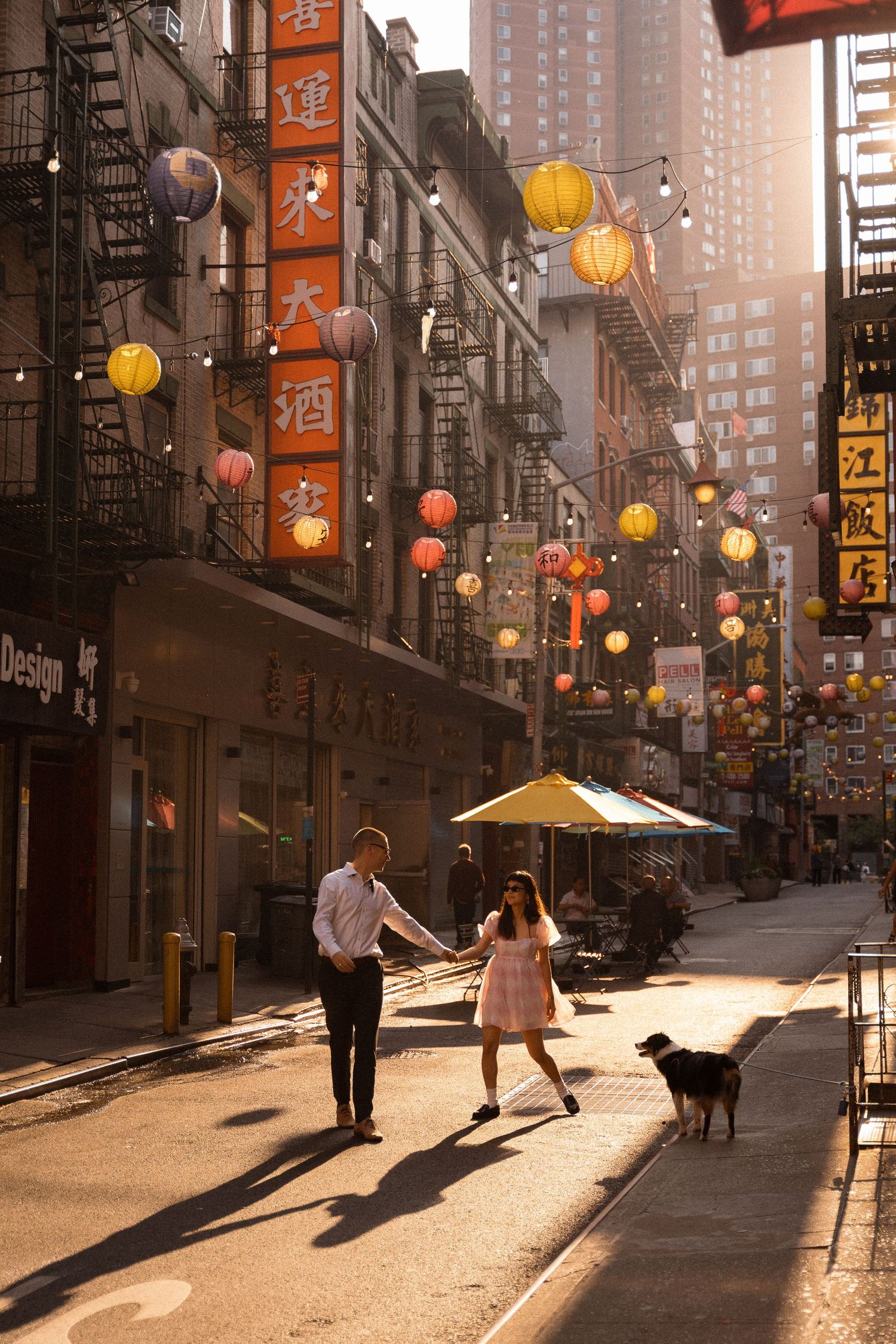 A street in Chinatown with hanging lanterns and long shadows cast by evening light.