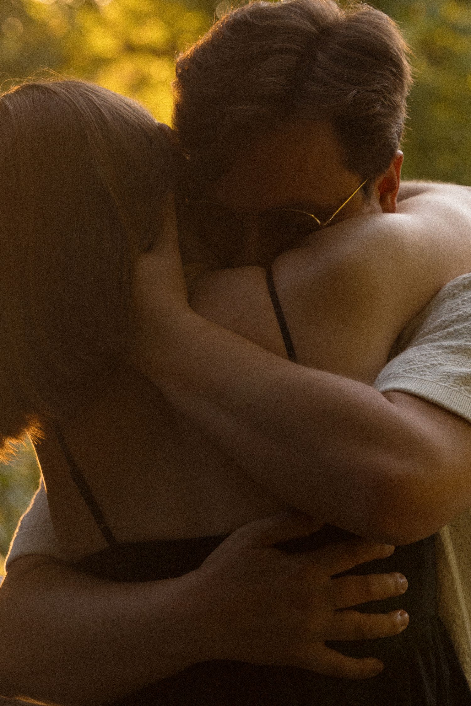 A romantic embrace captured in golden sunset lighting through trees.